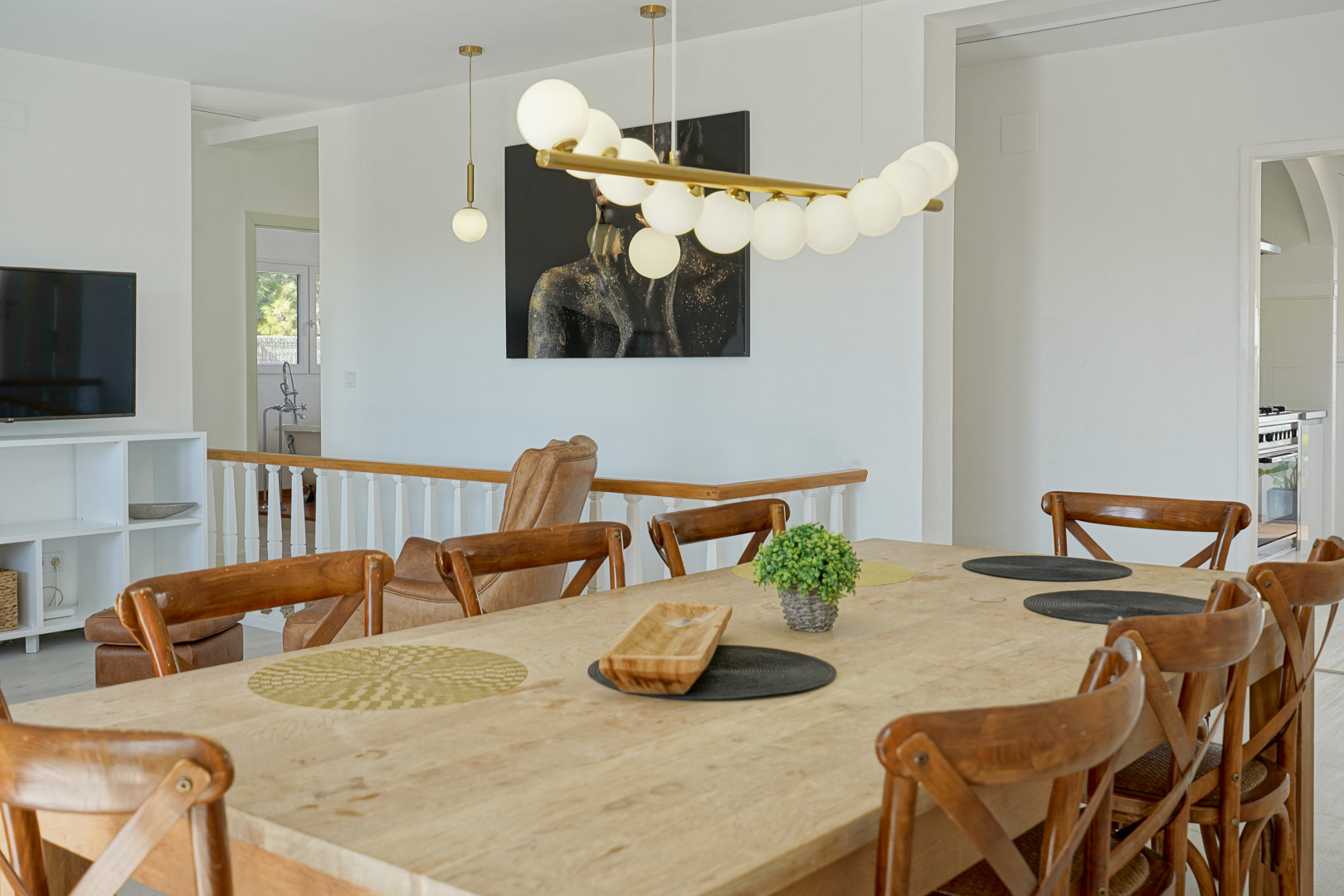 Comedor luminoso con mesa de madera natural y sillas de estilo rústico moderno, iluminado por una lámpara de diseño contemporáneo junto a la escalera.