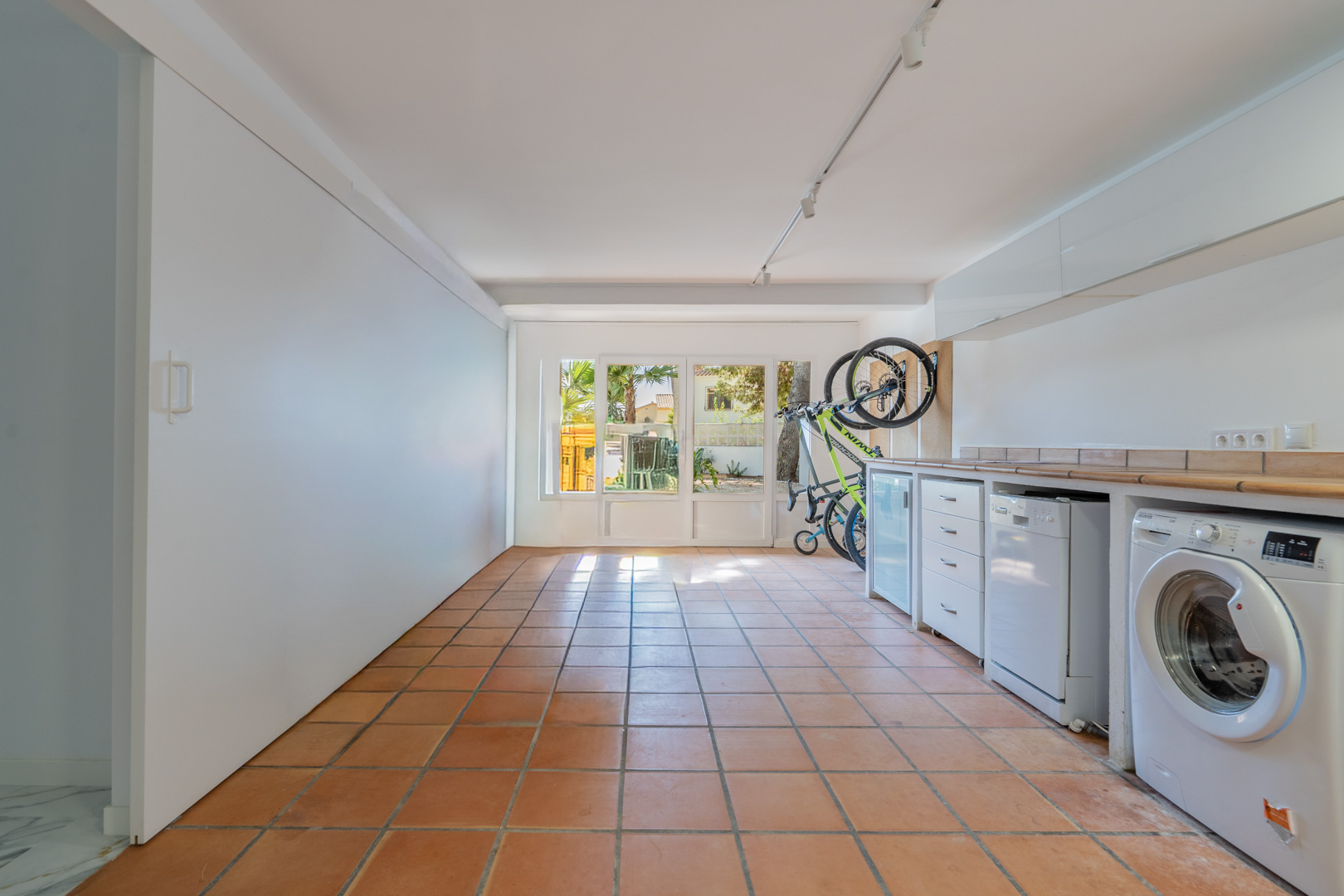 Garaje habilitado como zona de lavandería y trastero con suelos de terracota, encimera de azulejos, electrodomésticos integrados y acceso directo al exterior.