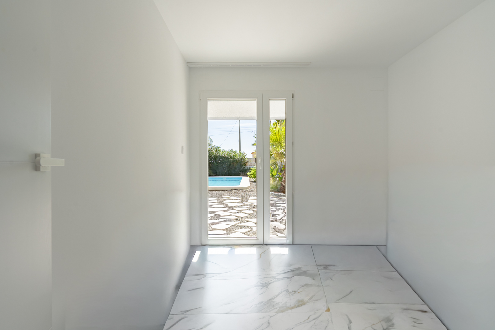 Habitación luminosa con suelos de gres porcelánico efecto mármol y acceso directo a la terraza de la piscina a través de una puerta acristalada.