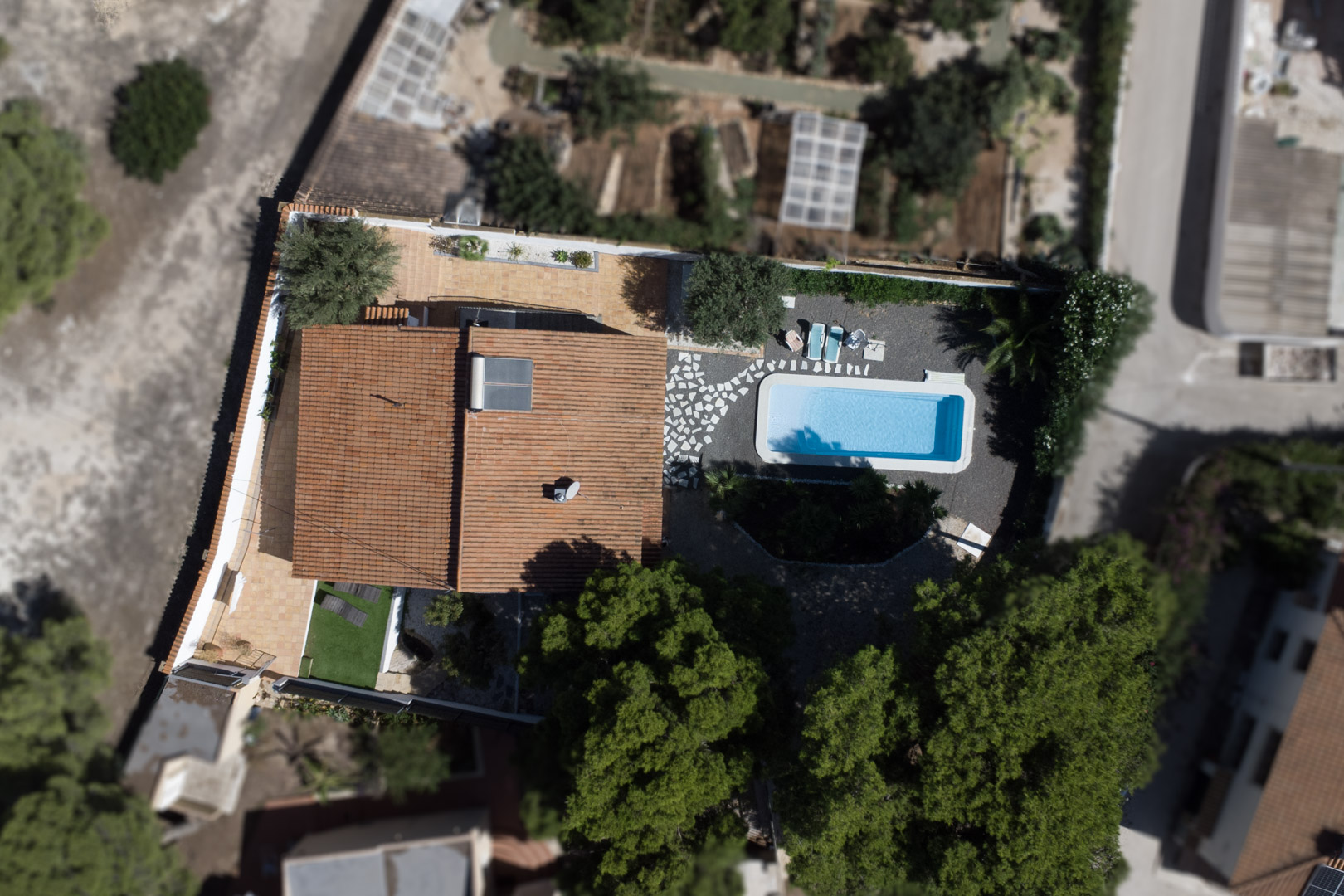 Vista aérea cenital de la propiedad que muestra la distribución de la parcela, la piscina rectangular, las terrazas de terracota y el panel solar en el tejado.