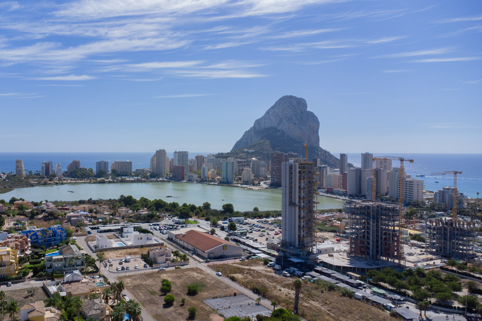 Vista panorámica elevada de Calpe que muestra el Peñón de Ifach, la laguna de Las Salinas y el perfil urbano costero bajo un cielo despejado.