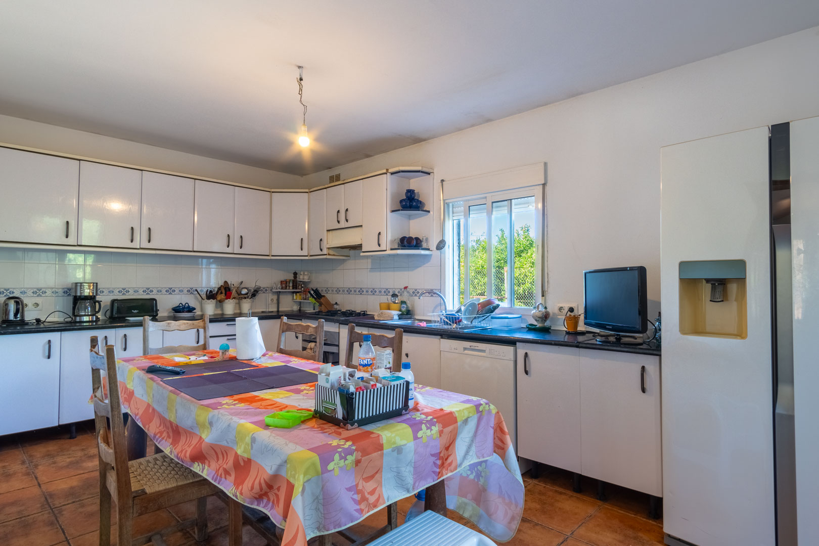 Cocina independiente con mobiliario blanco, encimera oscura y zona de comedor. Dispone de suelos cerámicos, ventana al exterior y equipamiento funcional.