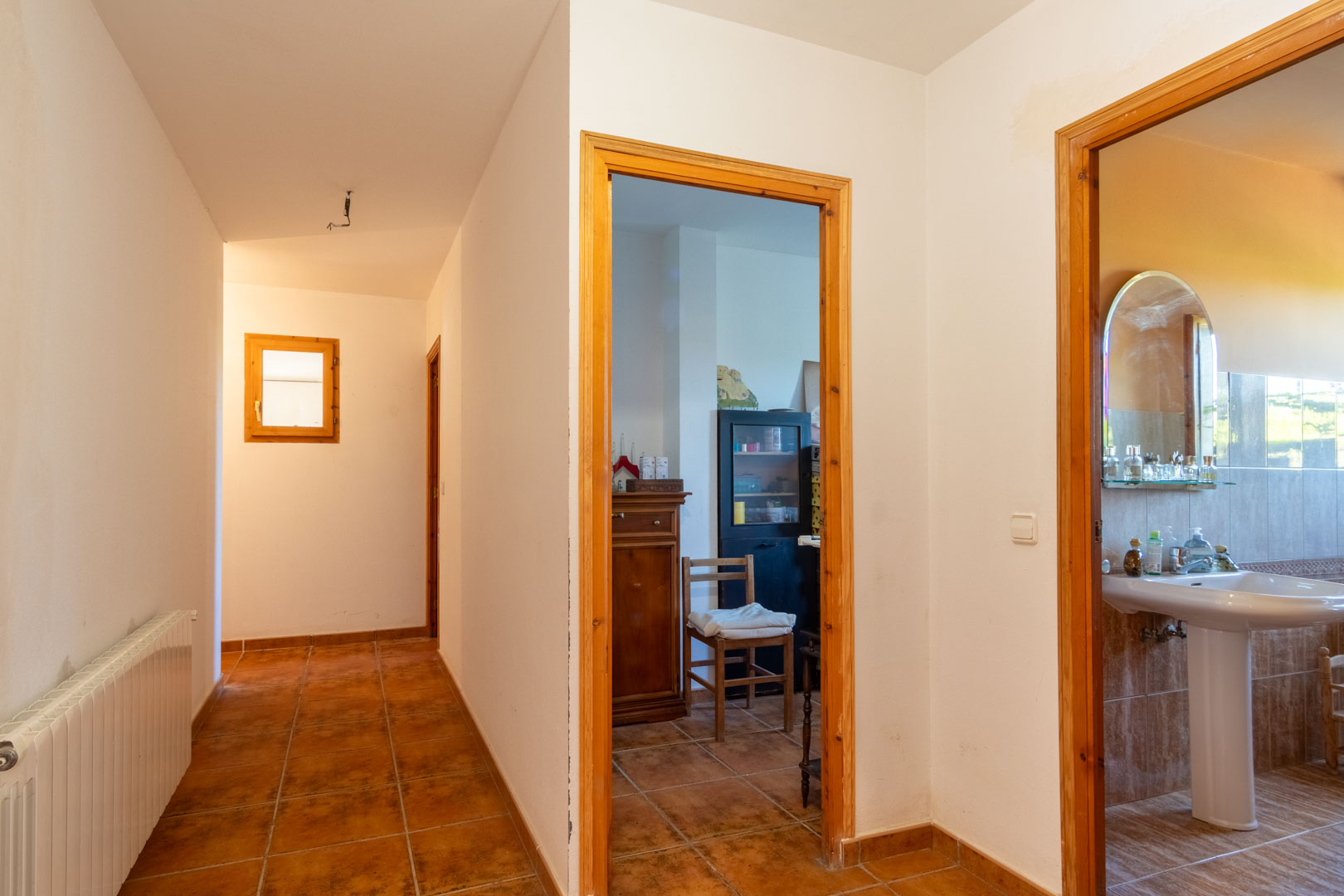 Pasillo distribuidor con suelos de gres rústico y carpintería de madera, que conecta con un baño completo y diversas estancias equipadas con calefacción por radiadores.