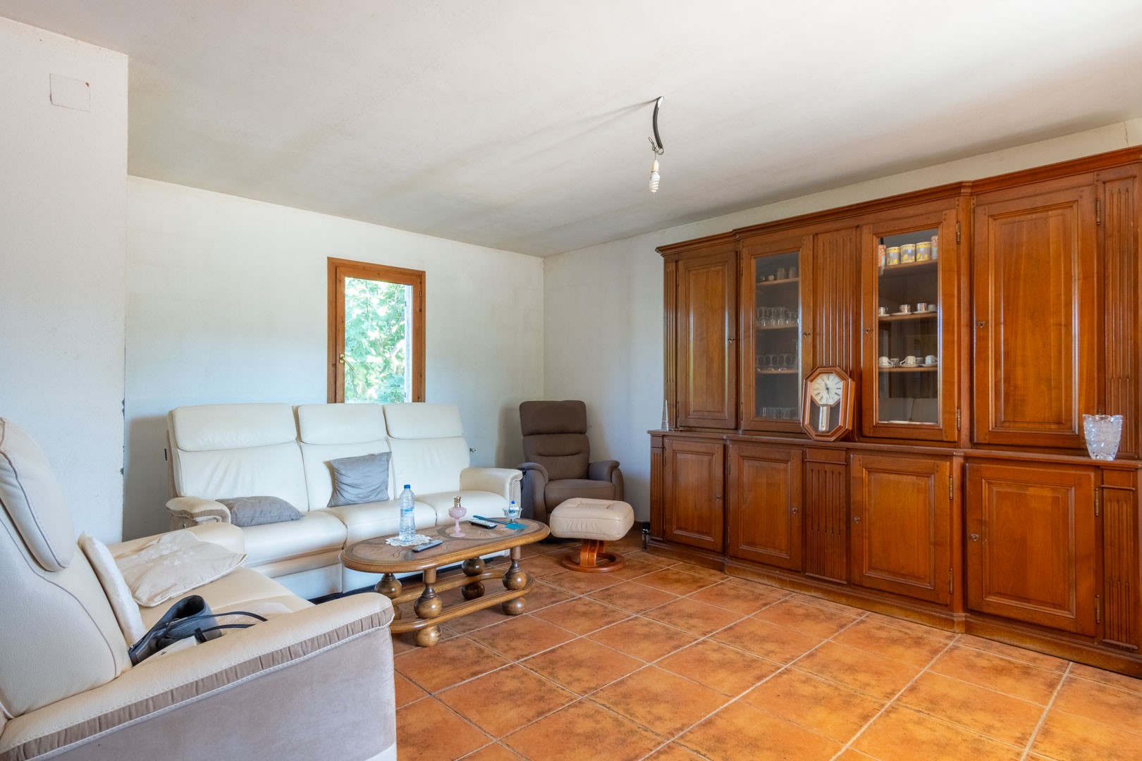 Salón con suelos de gres rústico, sofás de cuero blanco y un gran mueble de pared de madera maciza con vitrinas integradas.