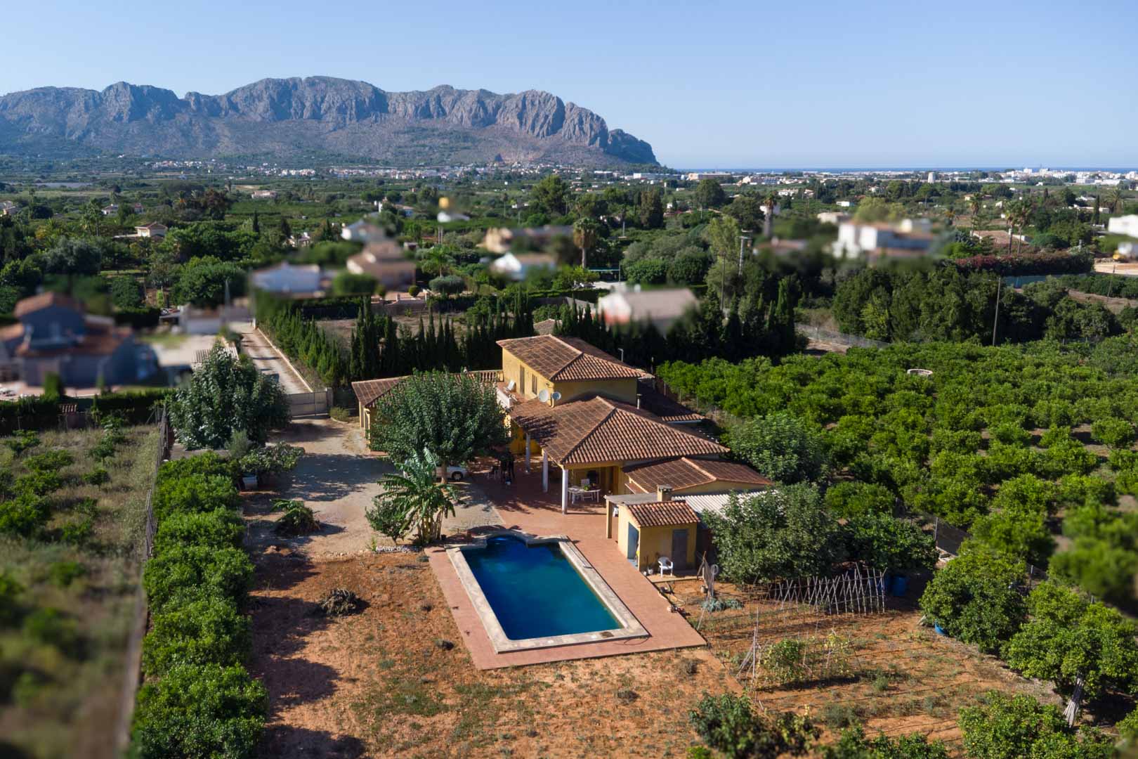 Vista aérea de la propiedad con tejados de teja cerámica, piscina privada y extensos huertos de cítricos frente a la majestuosa Sierra de Segaria.