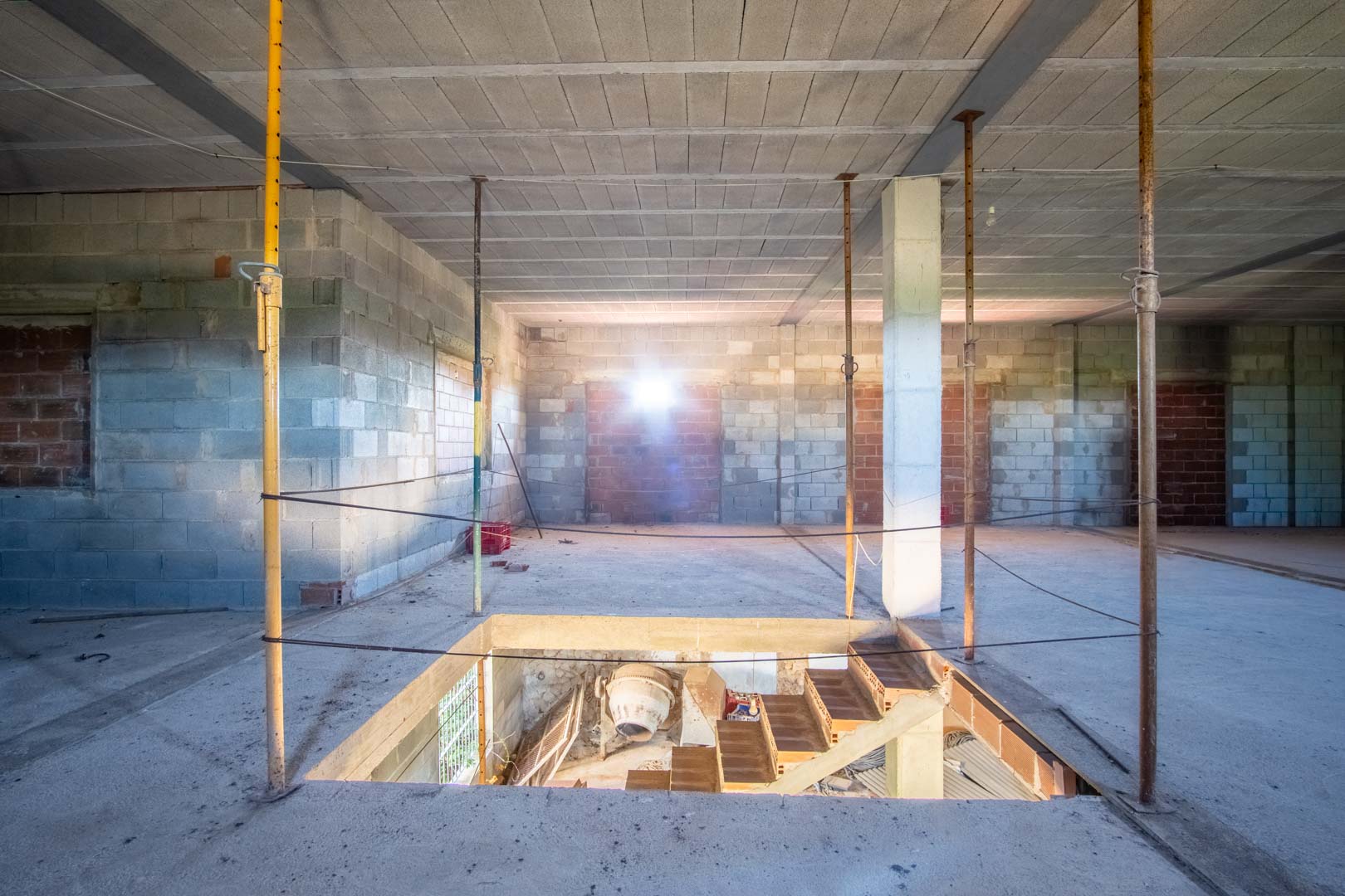 Interior diáfano en fase de construcción con muros de bloque, forjado de hormigón y hueco para escalera que conecta con la planta inferior.