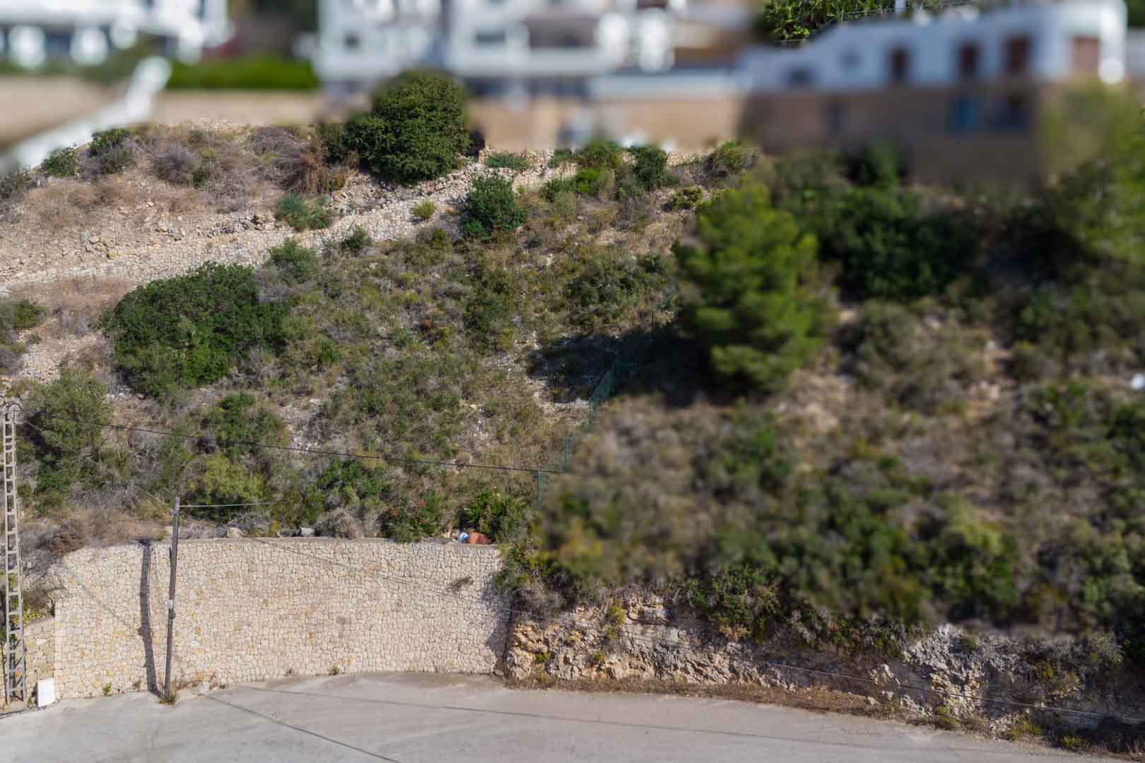 Parcela urbana elevada con muros de contención de piedra natural y vegetación autóctona, situada en una zona residencial consolidada de El Portet.