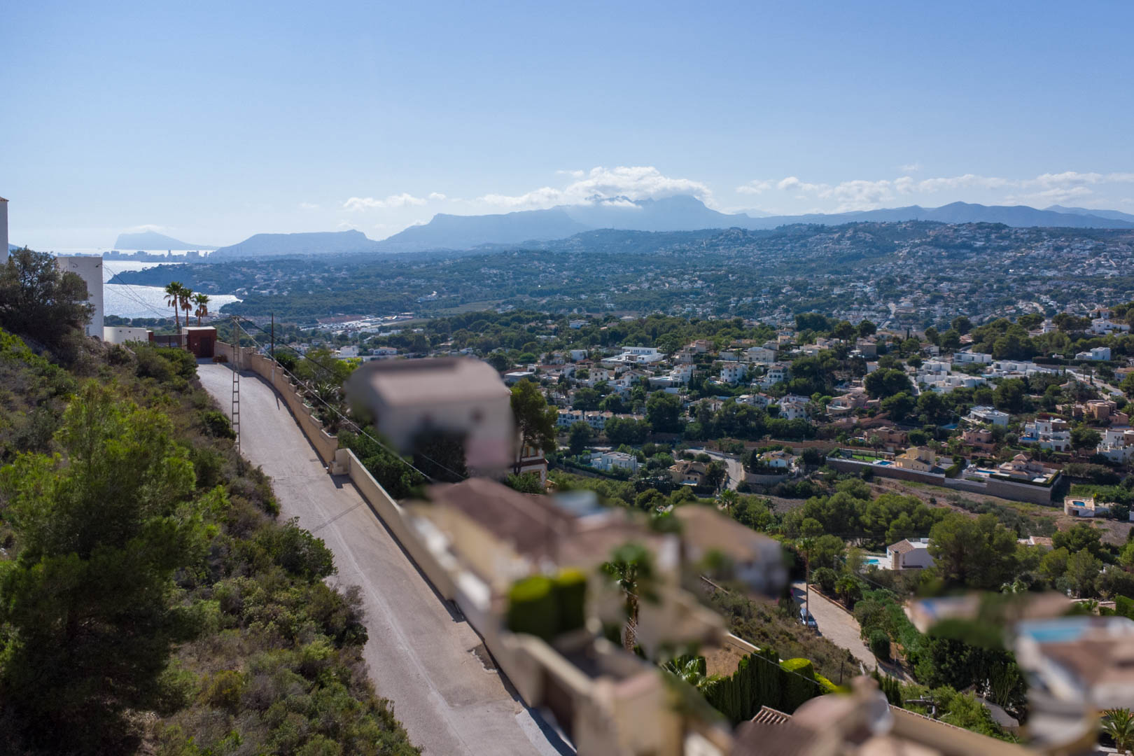 Vista panorámica desde la parcela elevada en El Portet, mostrando el entorno residencial, la costa de Moraira y las montañas al fondo bajo un cielo despejado.