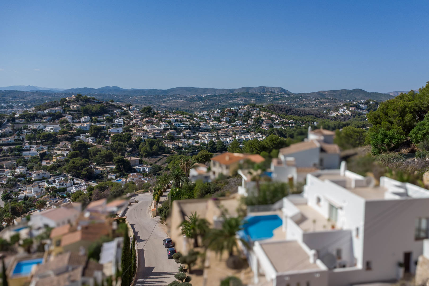 Vista panorámica elevada de la zona residencial de El Portet, destacando villas blancas con piscinas y el relieve montañoso bajo un cielo despejado.