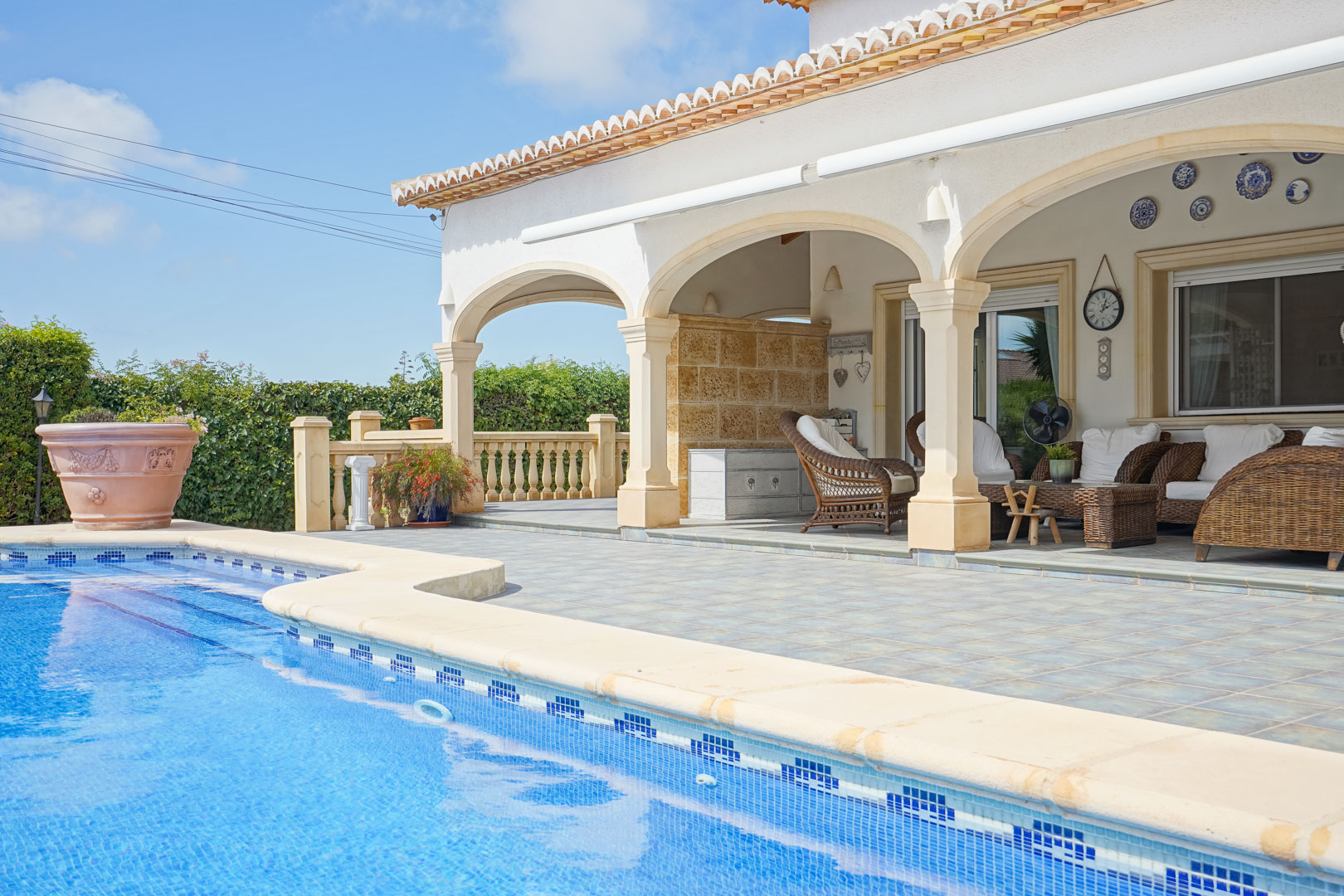 Vista de la piscina y terraza cubierta con arcos y mobiliario de mimbre en Jávea.