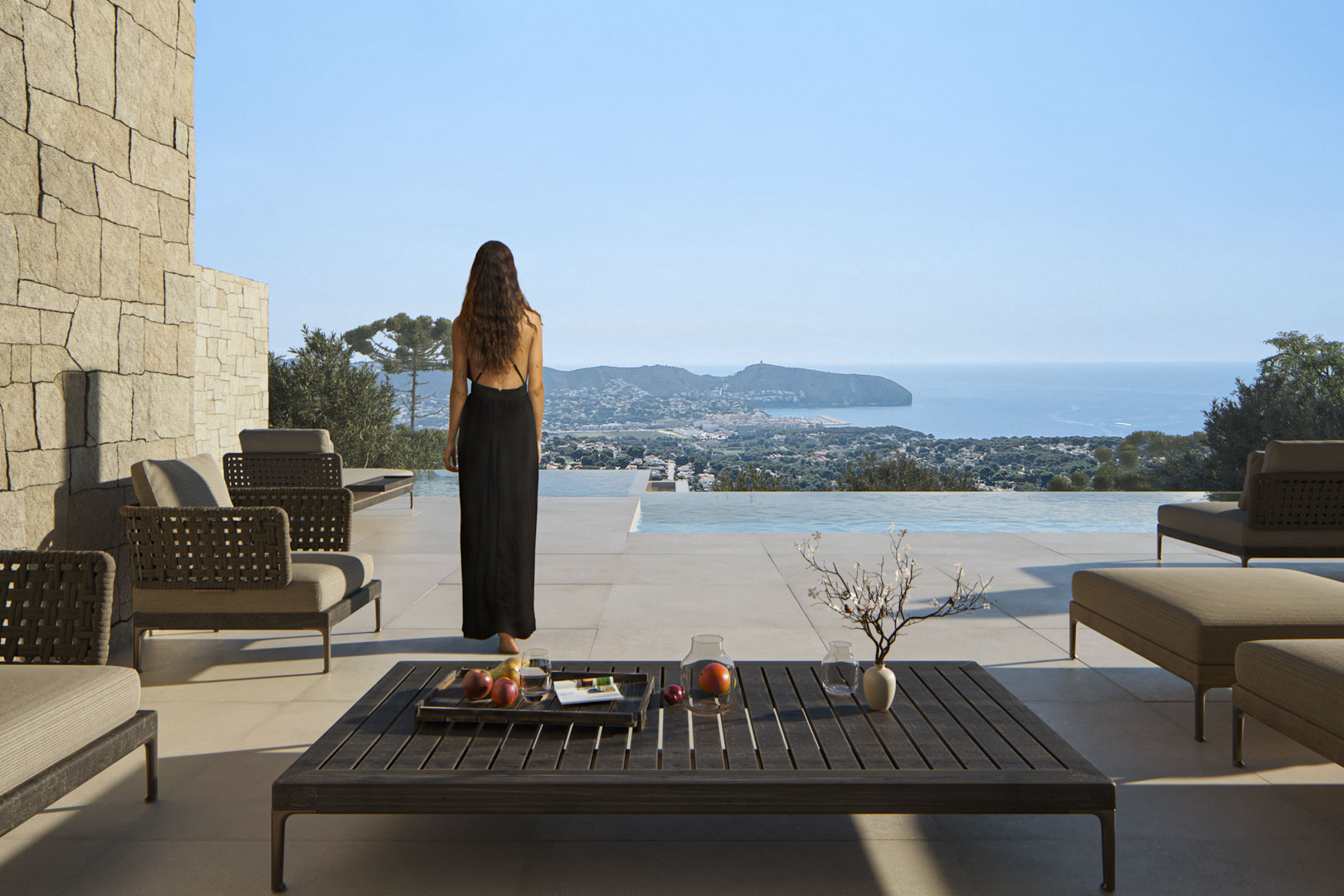 Terraza exterior con mobiliario de diseño, muro de piedra natural y piscina infinita con vistas panorámicas al mar Mediterráneo y la costa de Moraira.