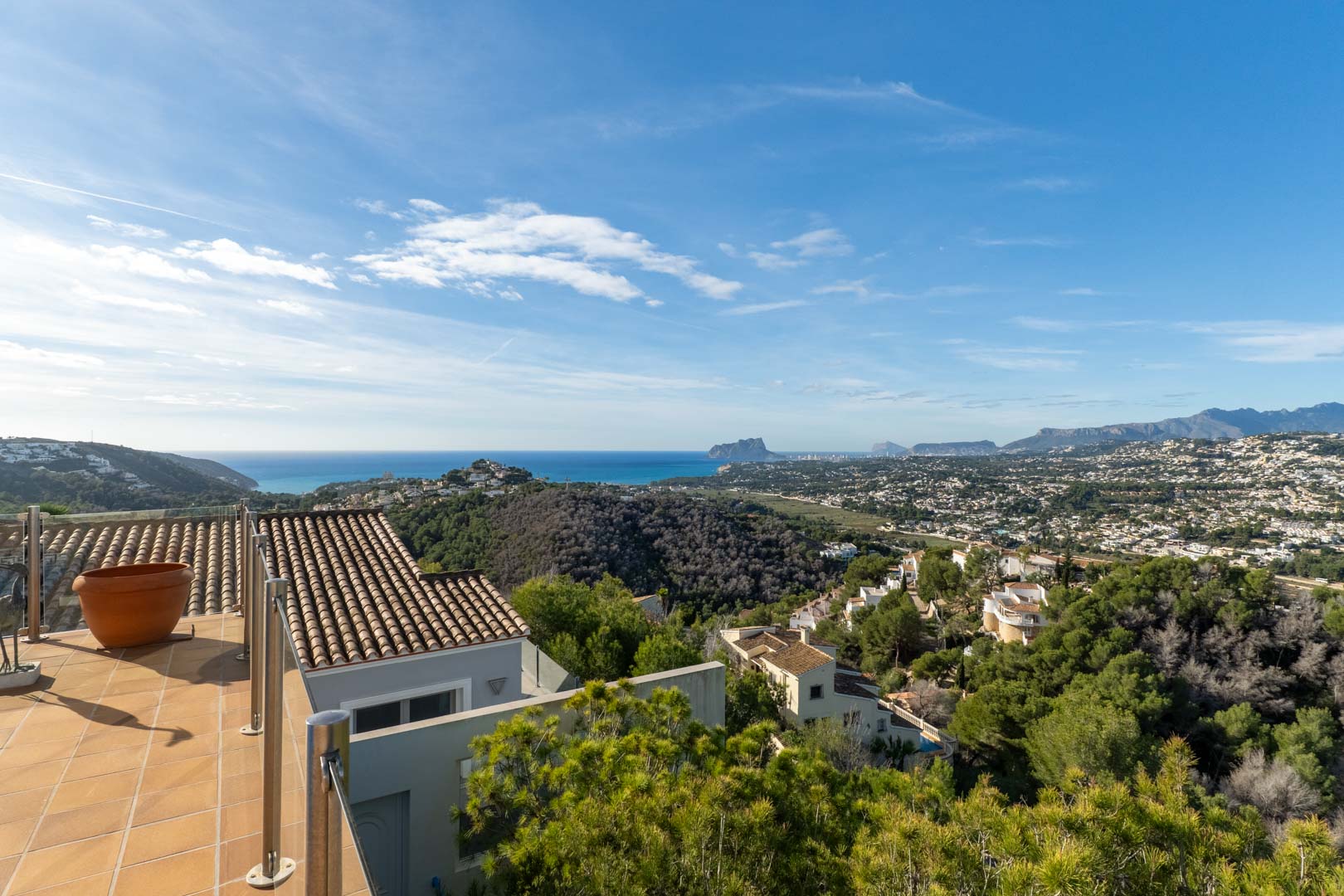 Terraza con suelo cerámico y barandilla de acero inoxidable que ofrece vistas panorámicas al mar Mediterráneo, el Peñón de Ifach y las montañas circundantes.