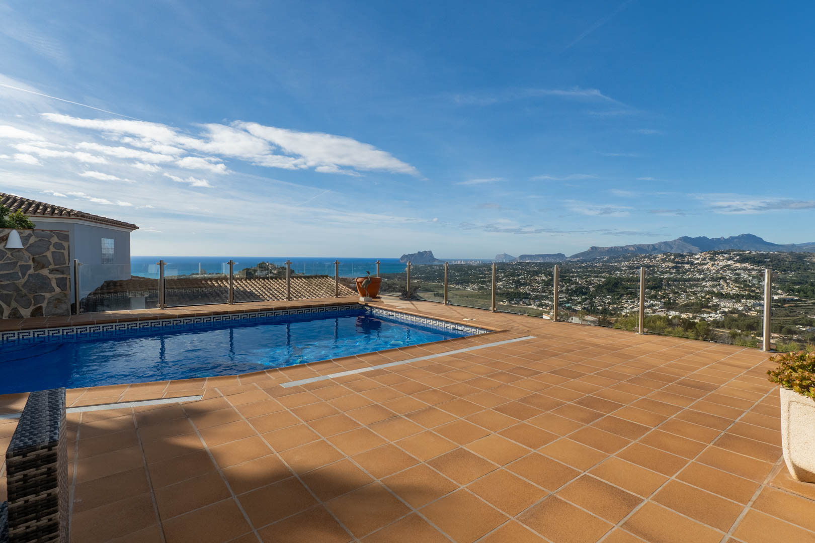 Terraza con suelo de terracota y piscina privada, protegida por barandillas de cristal que ofrecen vistas panorámicas al mar Mediterráneo y al Peñón de Ifach.