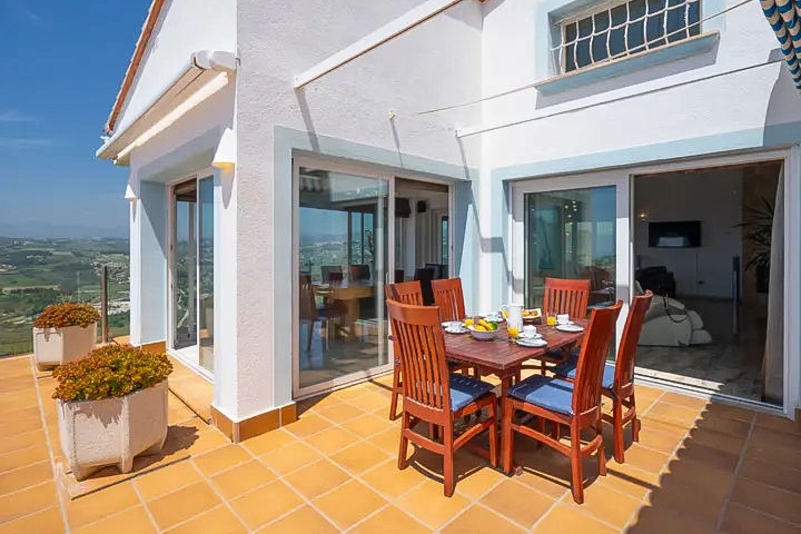Terraza exterior con suelo de gres cerámico, mesa de comedor de madera para seis personas y amplios ventanales que conectan con el interior de la villa.