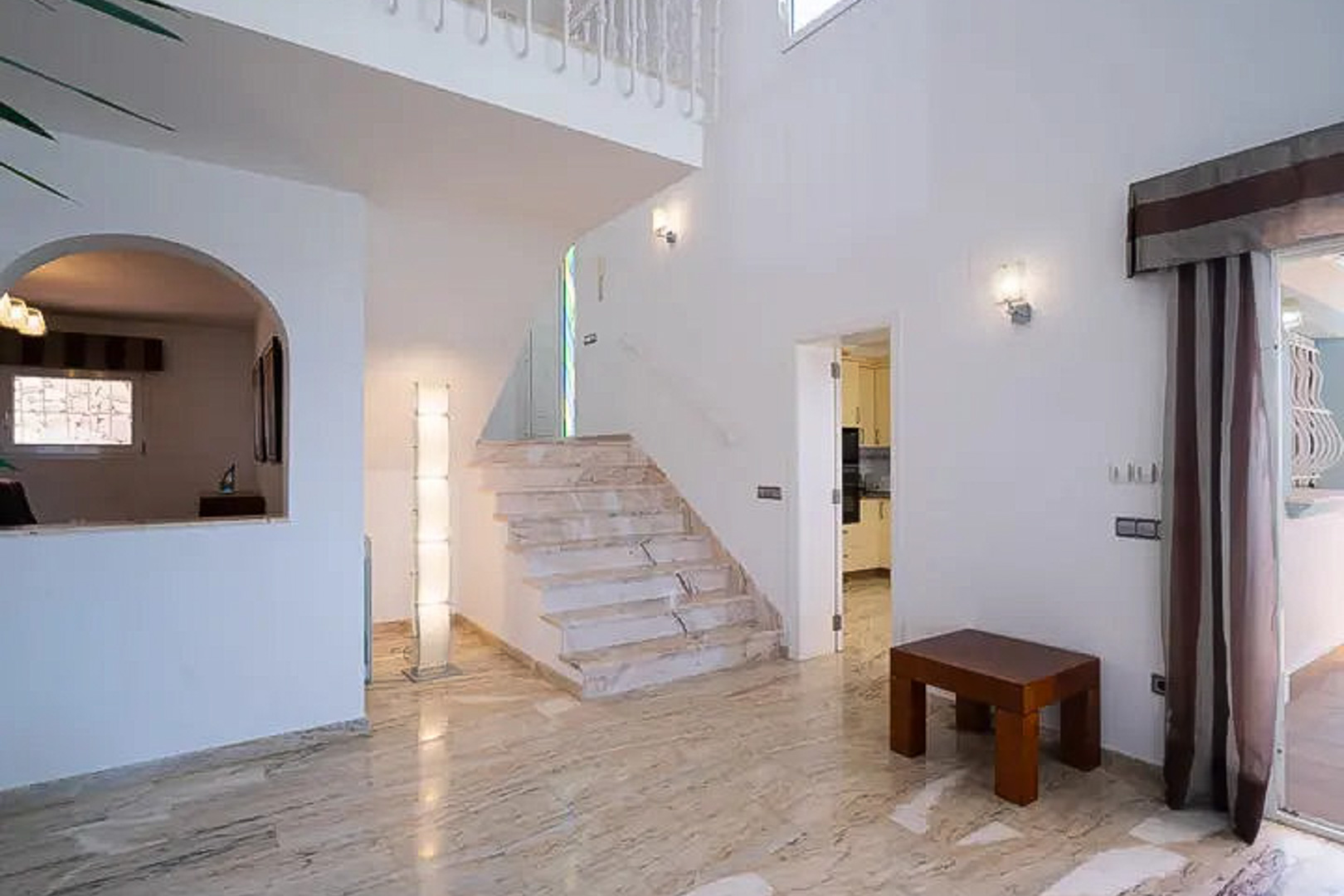 Vestíbulo de entrada con suelos de mármol pulido, escalera señorial y techos de doble altura que aportan amplitud y luminosidad natural a la vivienda.
