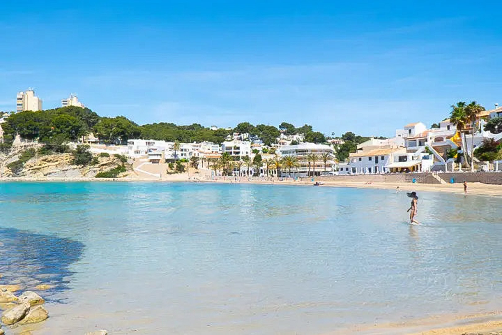 Vista panorámica de la Playa del Portet en Moraira, con sus aguas cristalinas poco profundas y la arquitectura blanca tradicional frente a la bahía.