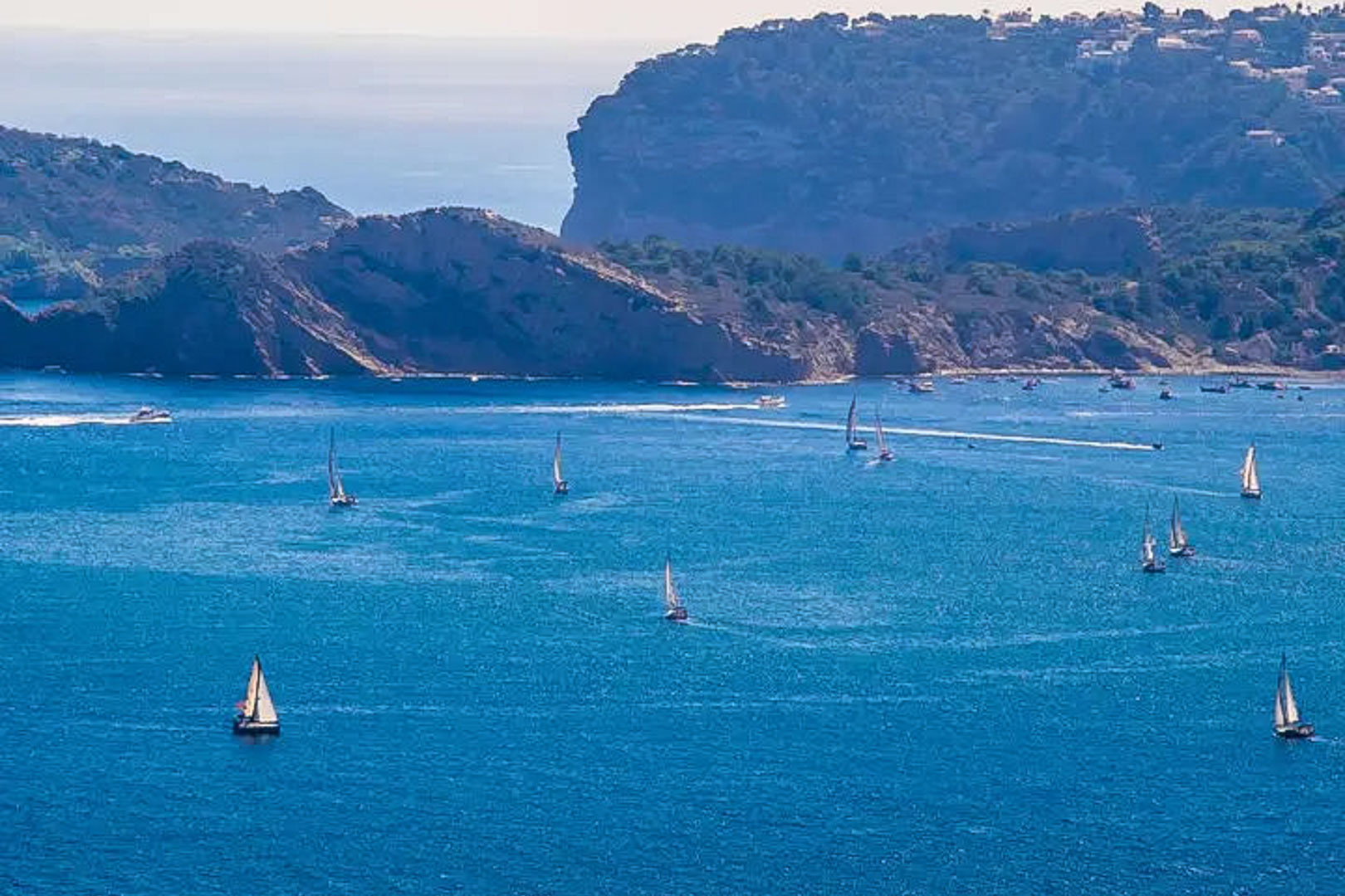 Vista panorámica del mar Mediterráneo en Moraira, con veleros navegando frente a los acantilados de la Costa Blanca bajo la luz natural del día.