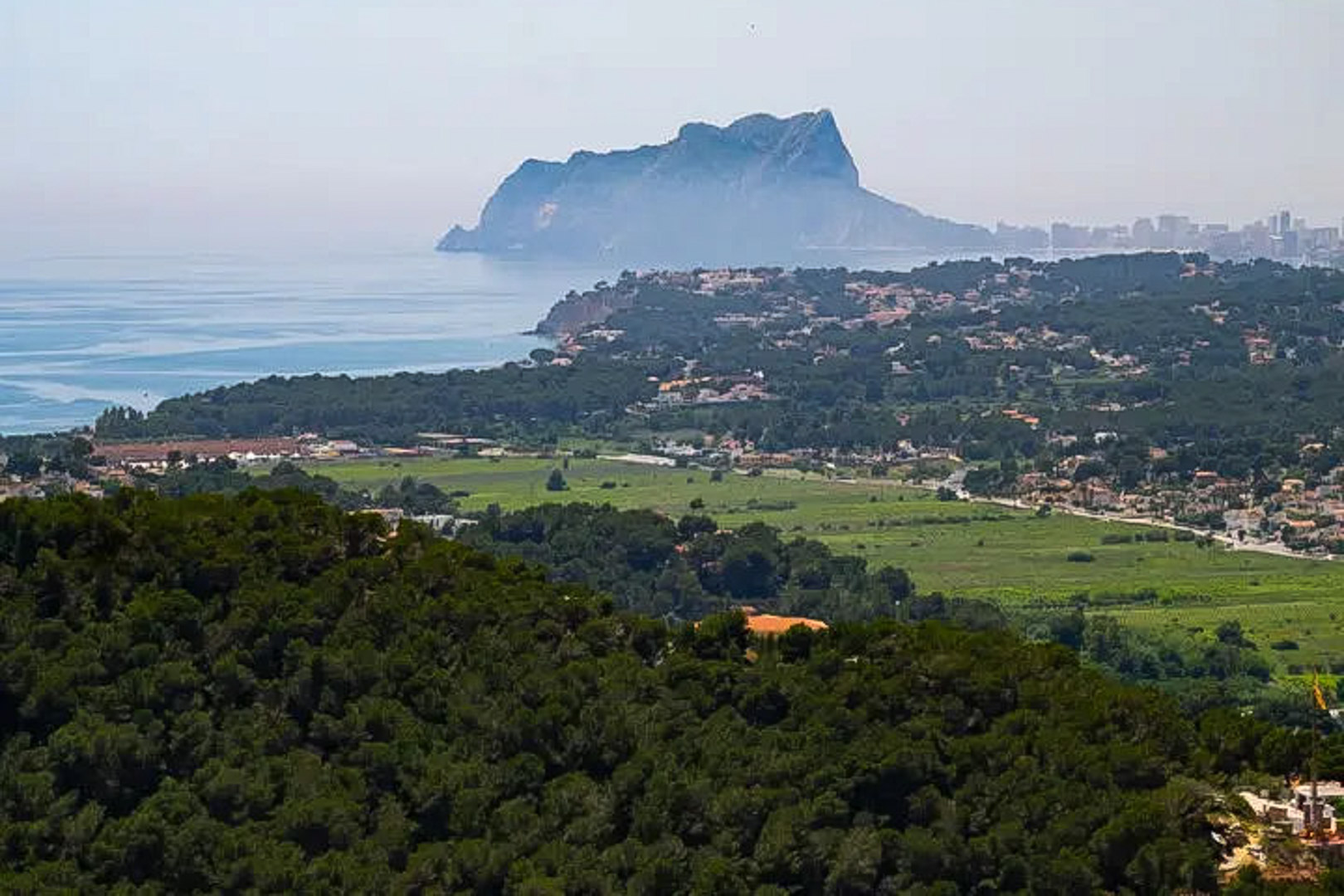 Vistas panorámicas hacia el Peñón de Ifach y la costa, destacando el contraste entre los densos bosques de pinos y el azul del mar Mediterráneo.