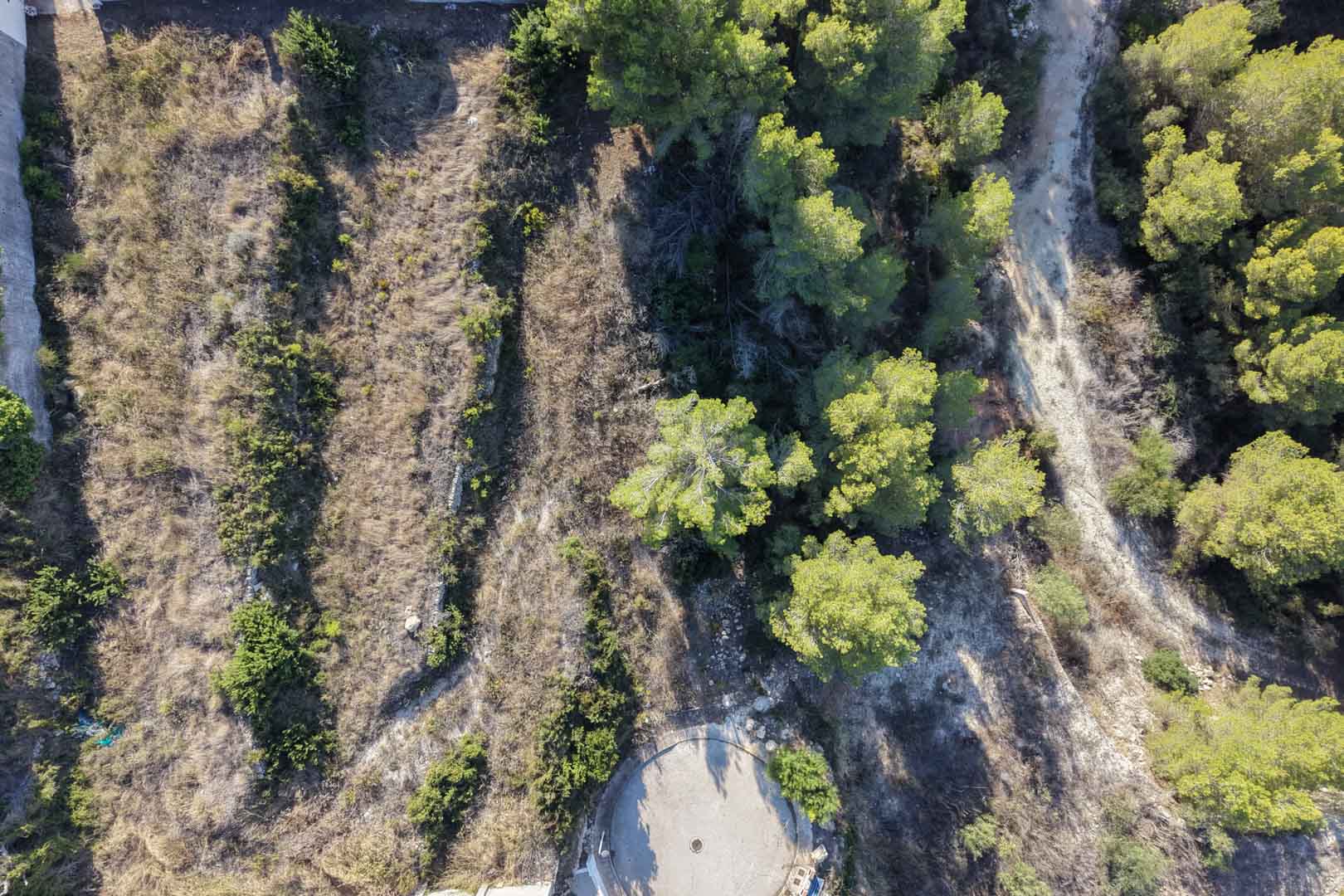 Vista aérea de la parcela urbana en Moraira, mostrando su topografía aterrazada con muros de piedra seca y vegetación mediterránea autóctona.