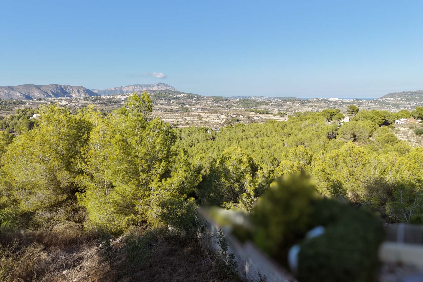 Vistas panorámicas desde la parcela en Benimeit, destacando el valle de pinos, las montañas en el horizonte y una franja del mar Mediterráneo bajo el cielo azul.