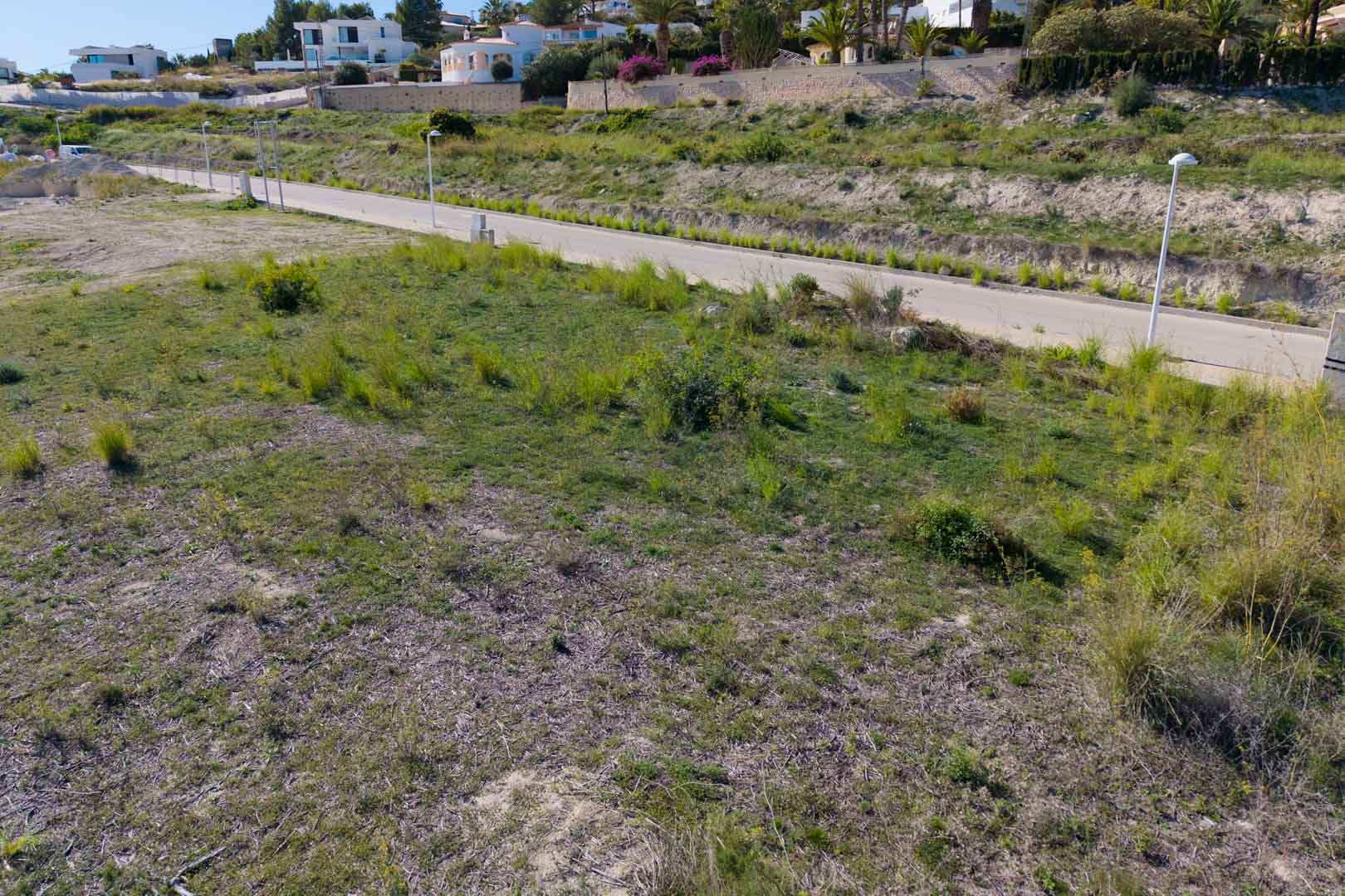 Parcela urbana llana con acceso directo desde calle asfaltada y alumbrado público, rodeada de villas modernas en la zona residencial de El Tesoro.