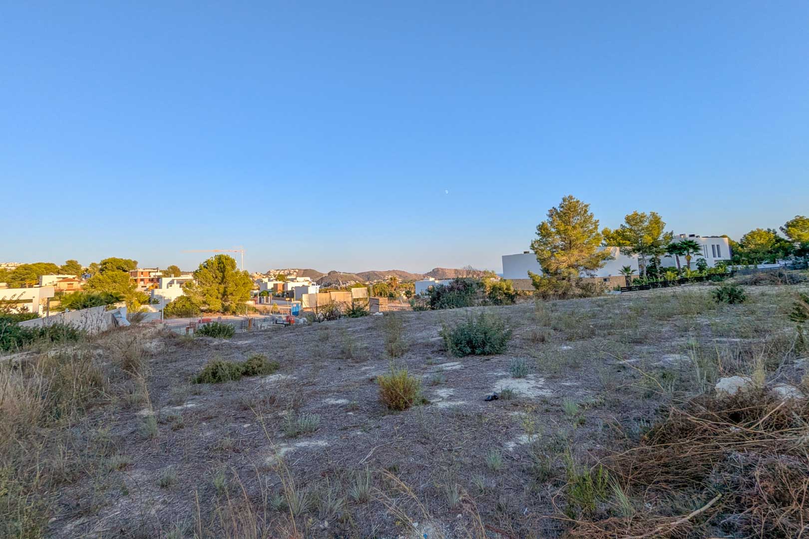 Parcela urbana llana en El Tesoro con vistas abiertas al valle y vegetación autóctona, rodeada de villas modernas en una zona residencial en desarrollo.