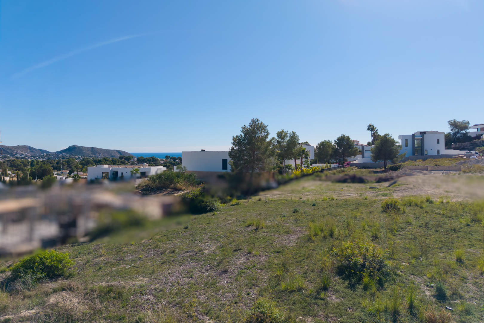 Parcela urbana llana en El Tesoro, Moraira, con vistas abiertas al valle y al mar Mediterráneo, rodeada de villas de diseño contemporáneo.