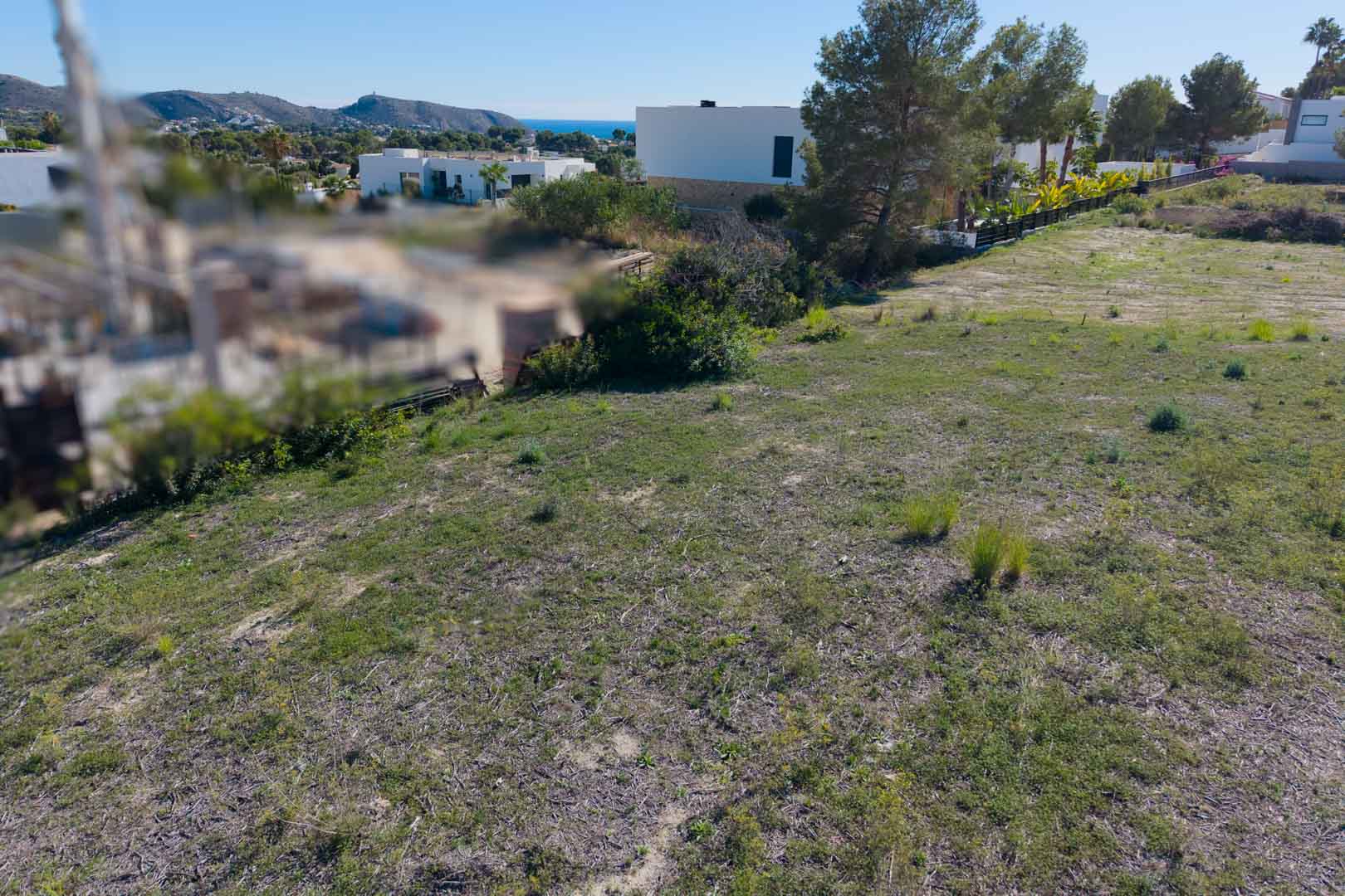 Parcela urbana llana en El Tesoro, Moraira, con vistas despejadas al valle y al mar Mediterráneo, rodeada de arquitectura moderna y pinos.