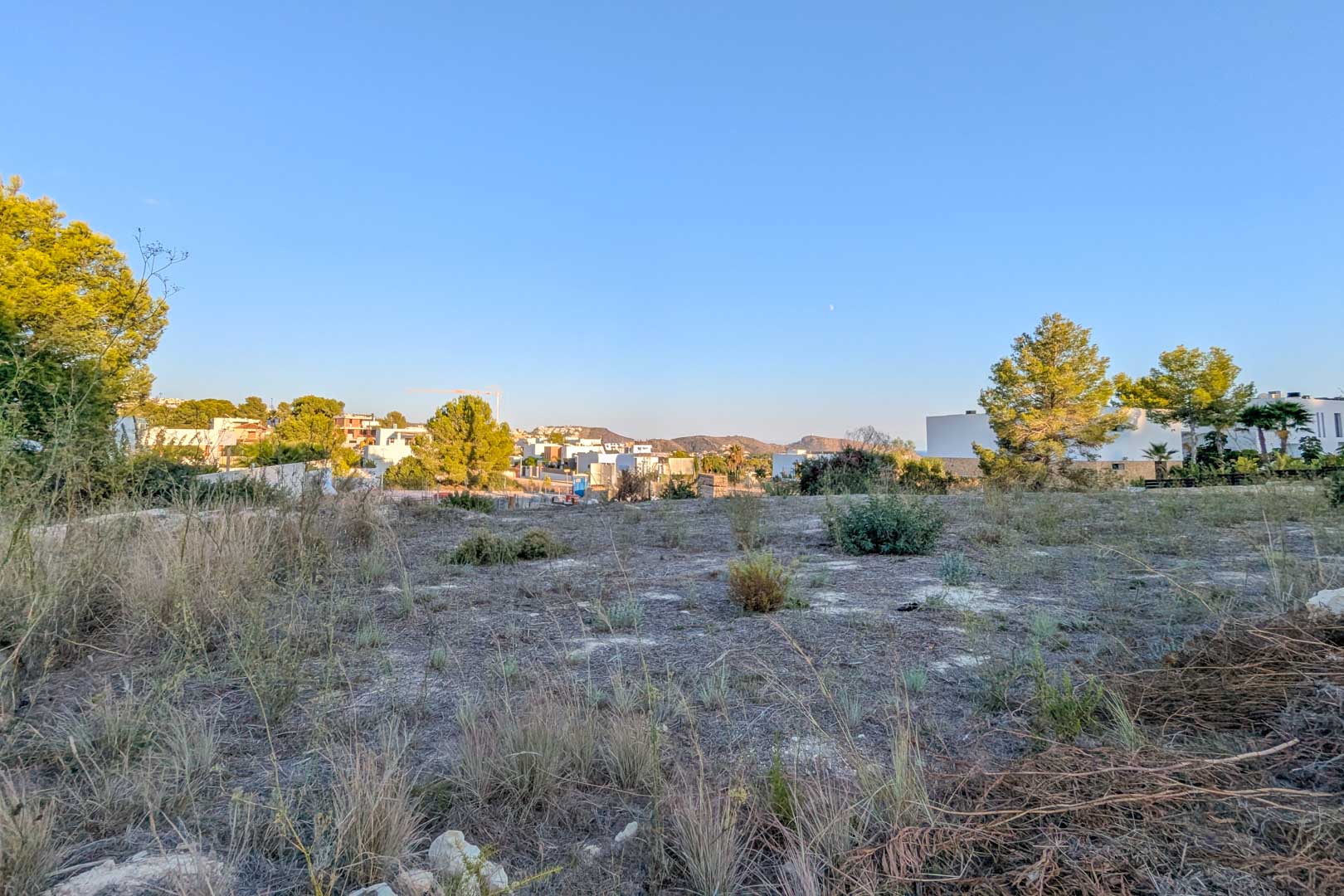 Vista panorámica de la parcela llana en El Tesoro, rodeada de vegetación mediterránea y modernas villas blancas bajo un cielo despejado.