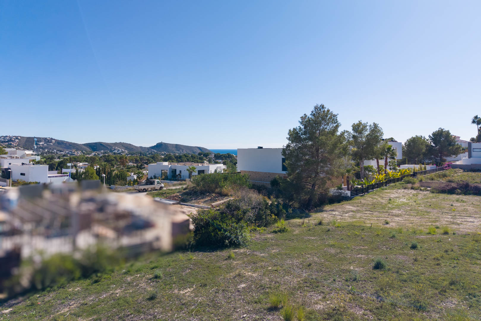 Vista panorámica desde la parcela urbana en El Tesoro, mostrando el terreno llano, villas modernas circundantes y vistas despejadas hacia el valle y el mar.