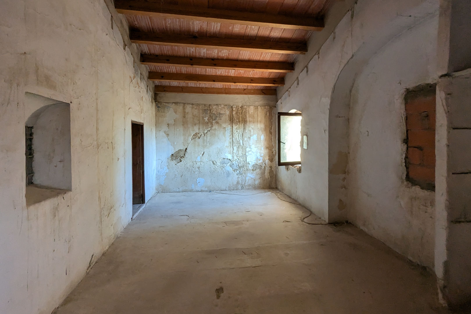 Amplia estancia diáfana con techos altos de vigas de madera y bovedillas de barro. Los gruesos muros muestran hornacinas originales y una ventana lateral que aporta luz natural.
