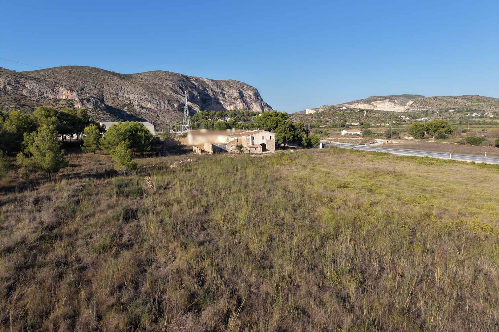 Vista panorámica de la casa de piedra tradicional situada en una extensa parcela rústica, rodeada de vegetación mediterránea y montañas en Teulada.