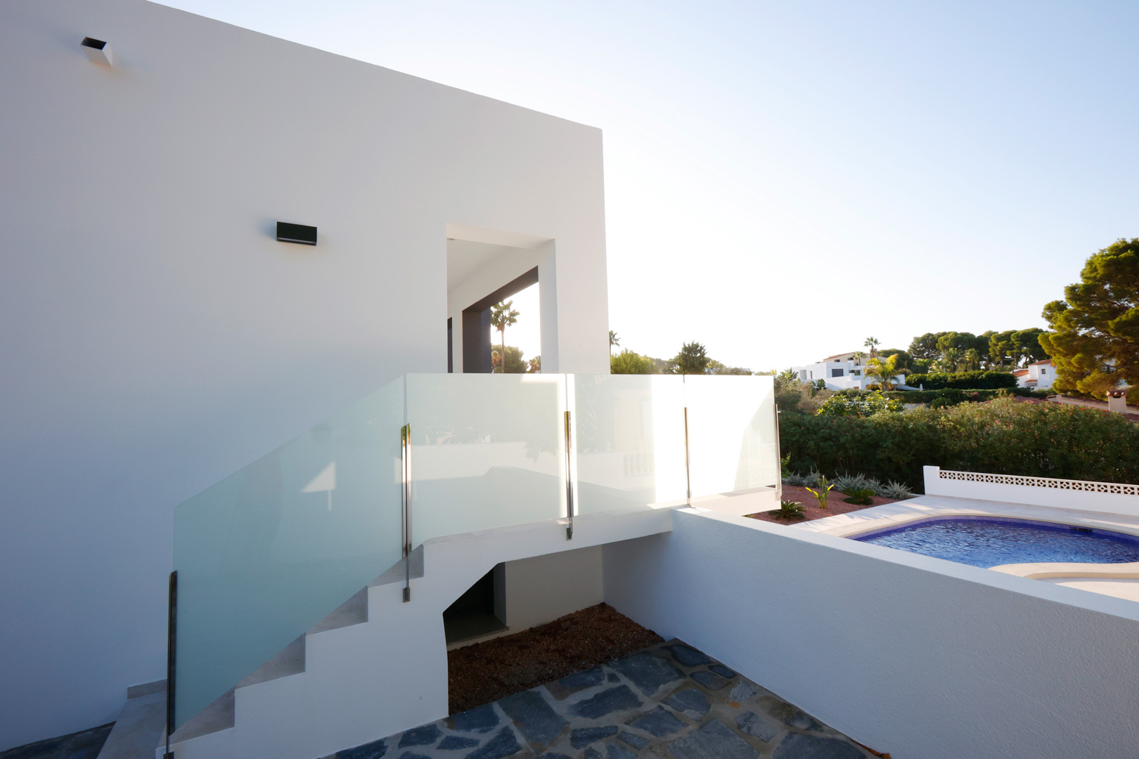 Escalera exterior con barandillas de acero y cristal que comunica la zona de la piscina con la entrada superior de la fachada blanca.