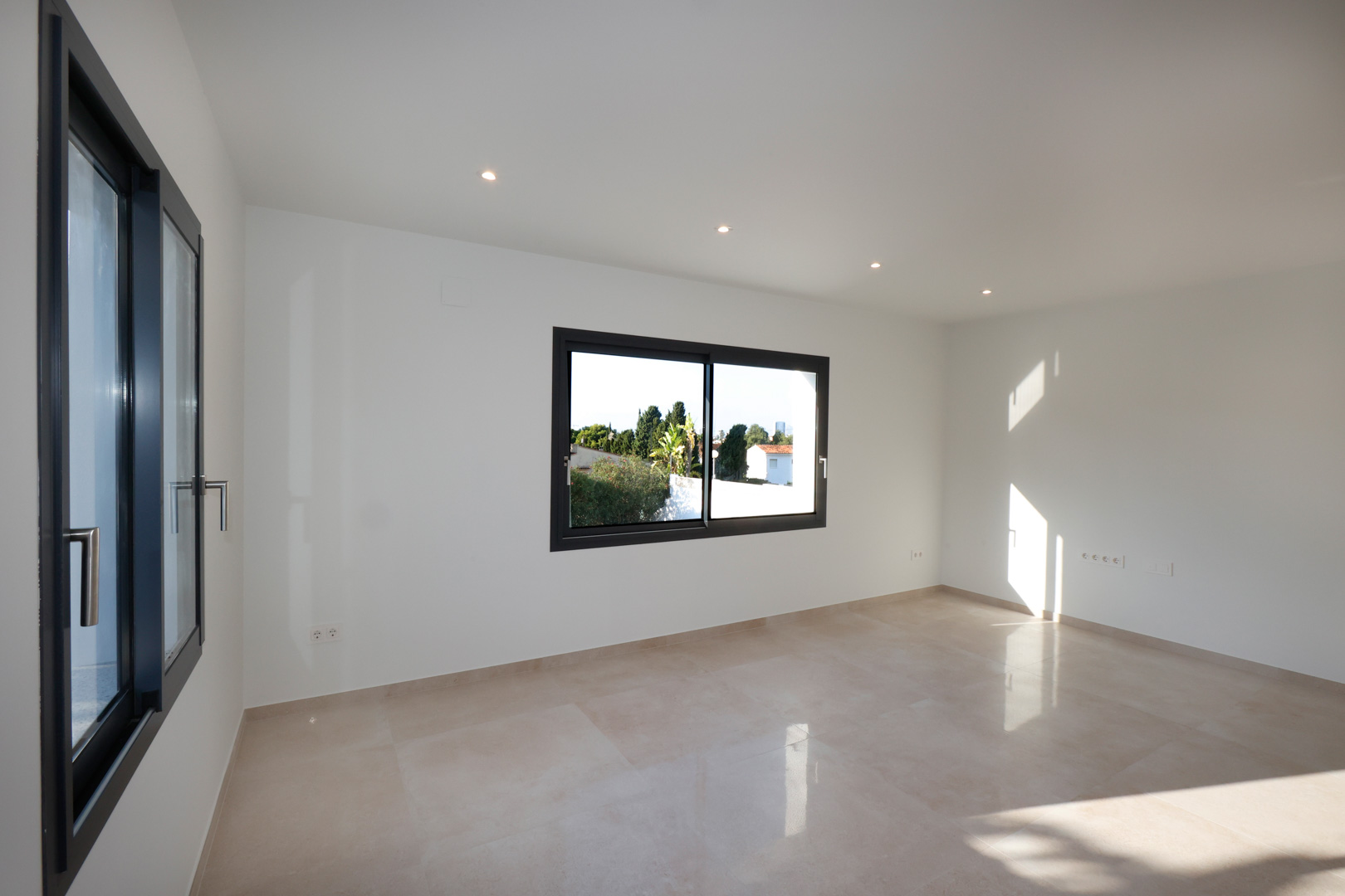 Habitación luminosa con suelo de gres porcelánico, carpintería Technal en gris antracita e iluminación LED integrada en el techo.