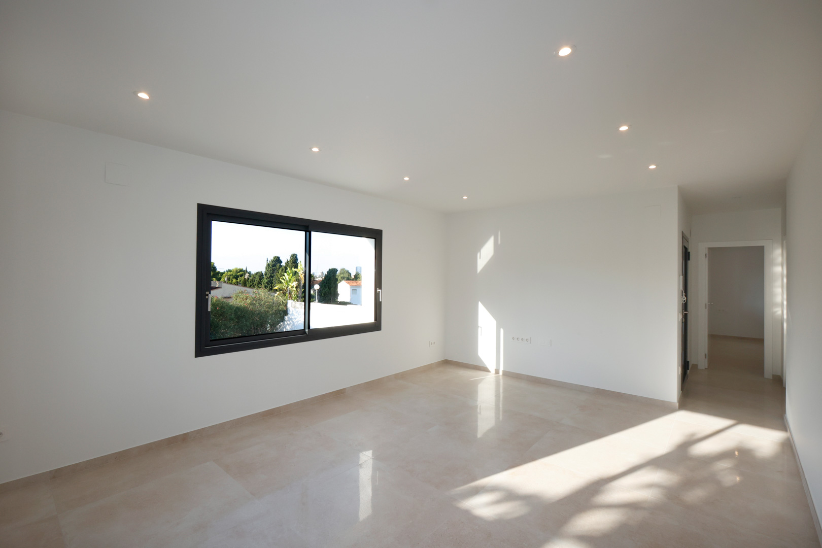 Salón luminoso con suelo de gres porcelánico, iluminación LED empotrada y ventanal Technal. El espacio conecta con un pasillo que incluye el sistema de videoportero.