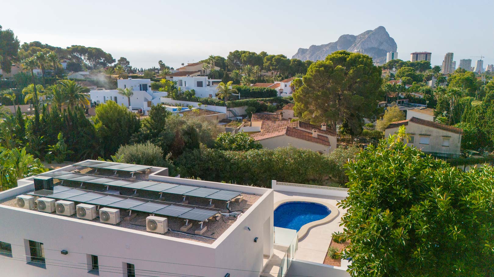 Vista aérea que muestra la instalación solar fotovoltaica en la cubierta, la piscina privada y las vistas panorámicas hacia el Peñón de Ifach.
