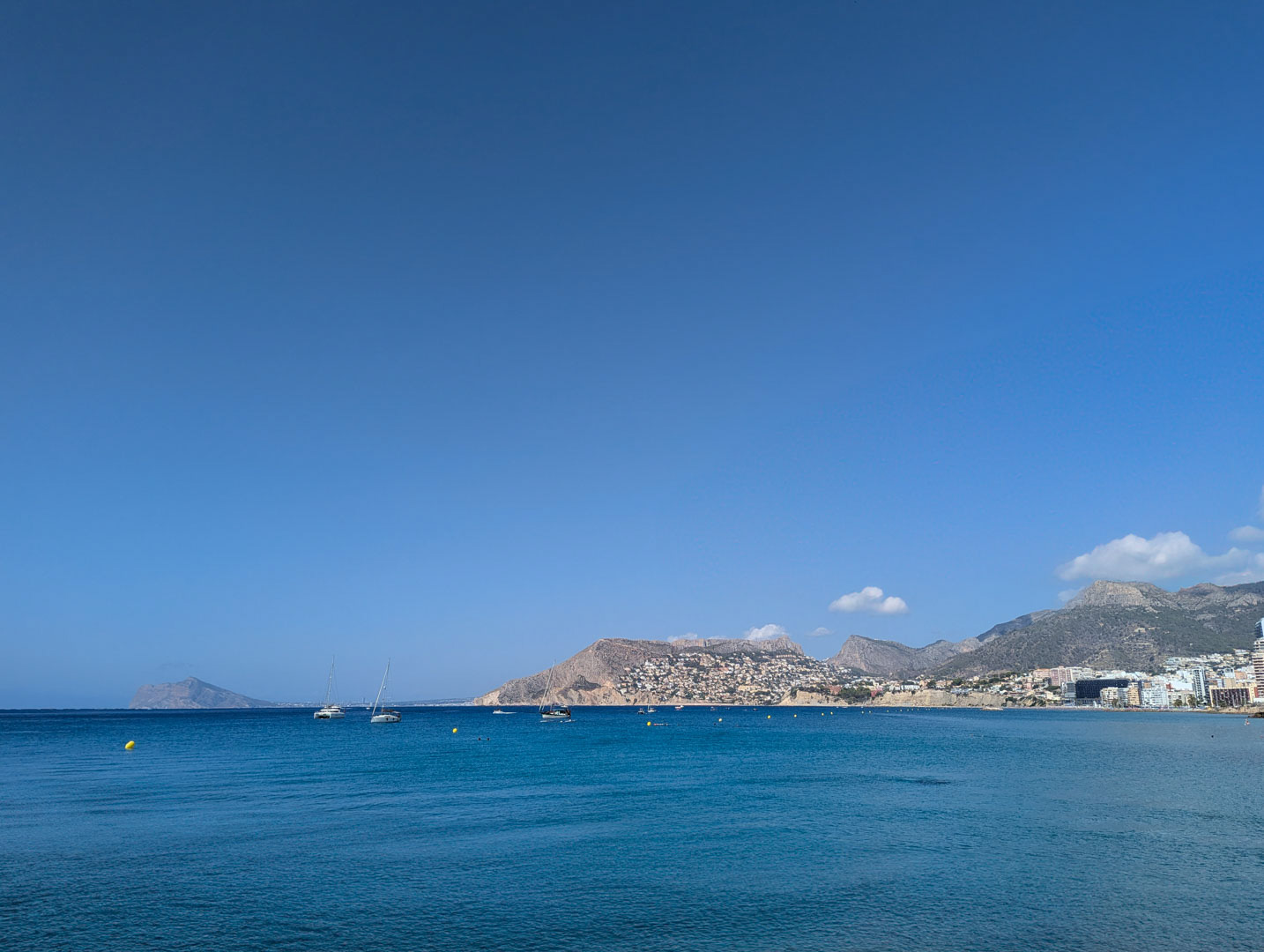 Vistas panorámicas del mar Mediterráneo y la costa montañosa con embarcaciones fondeadas bajo un cielo azul despejado.