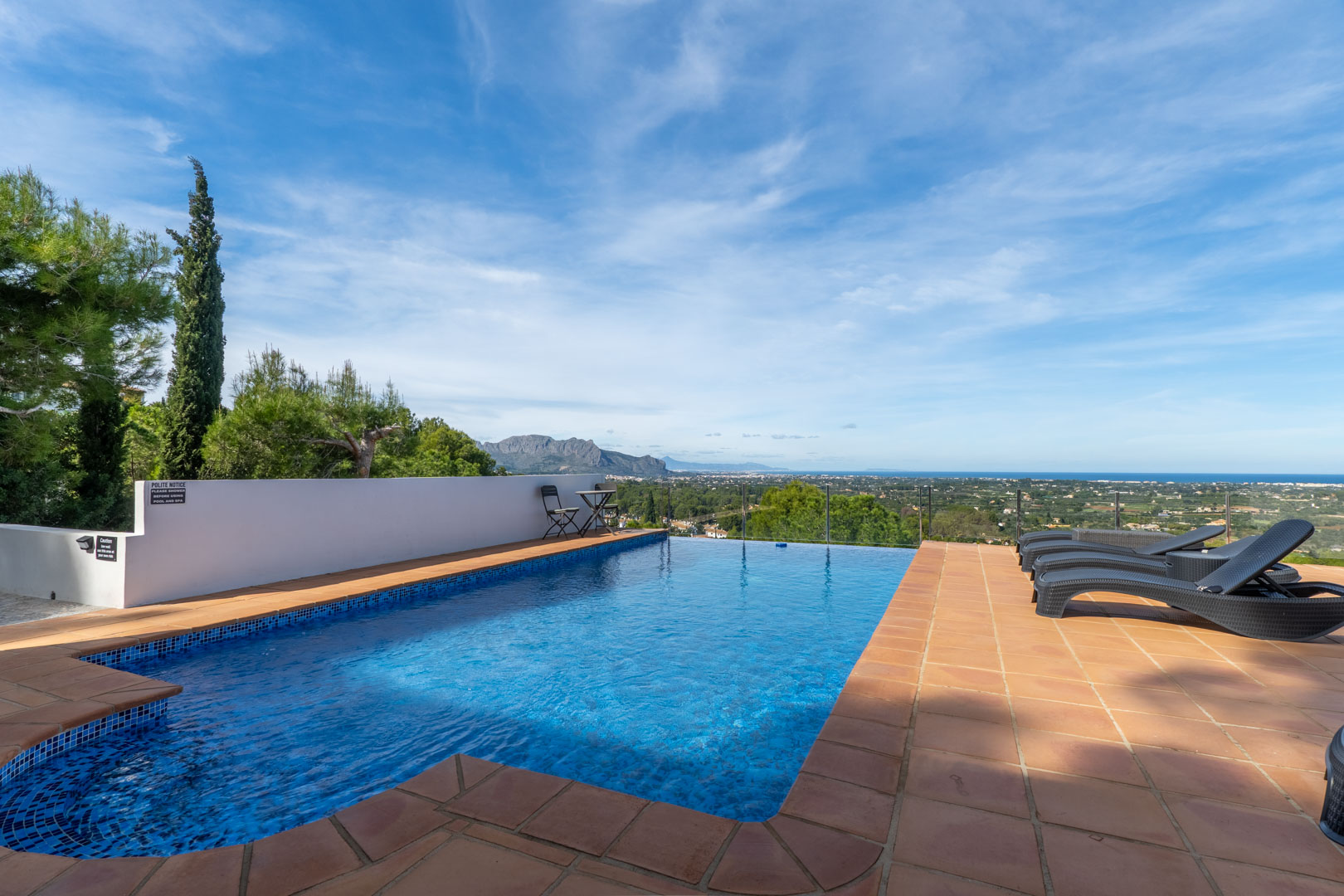 Piscina con revestimiento de mosaico azul y terraza de terracota, ofreciendo vistas panorámicas al mar Mediterráneo y al macizo del Montgó.