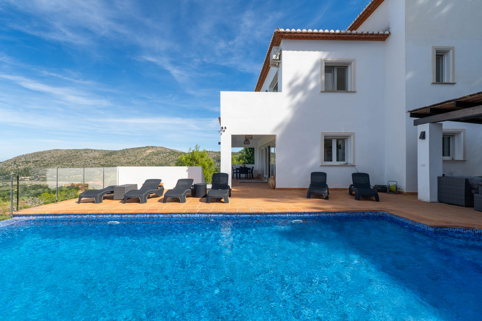 Piscina privada con revestimiento de mosaico azul, rodeada de una amplia terraza de terracota con tumbonas y vistas despejadas a las montañas en La Sella.