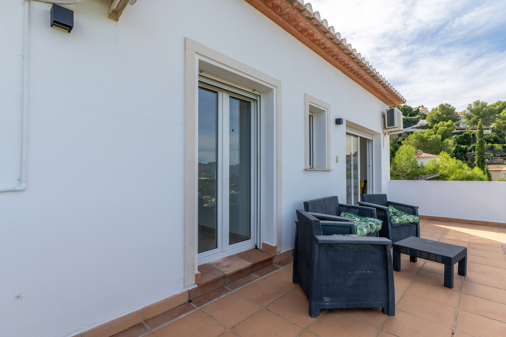 Terraza superior con suelo de barro cocido, mobiliario de exterior en ratán sintético y acceso directo a los dormitorios mediante ventanales de doble acristalamiento.