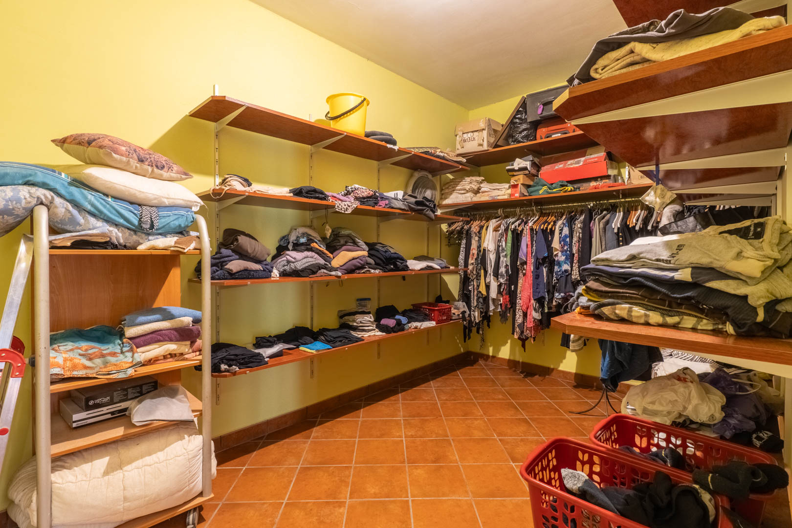 Vestidor funcional con estanterías de madera perimetrales, zona de colgado y suelo de gres rústico en tonos terracota, ofreciendo un amplio espacio de organización.