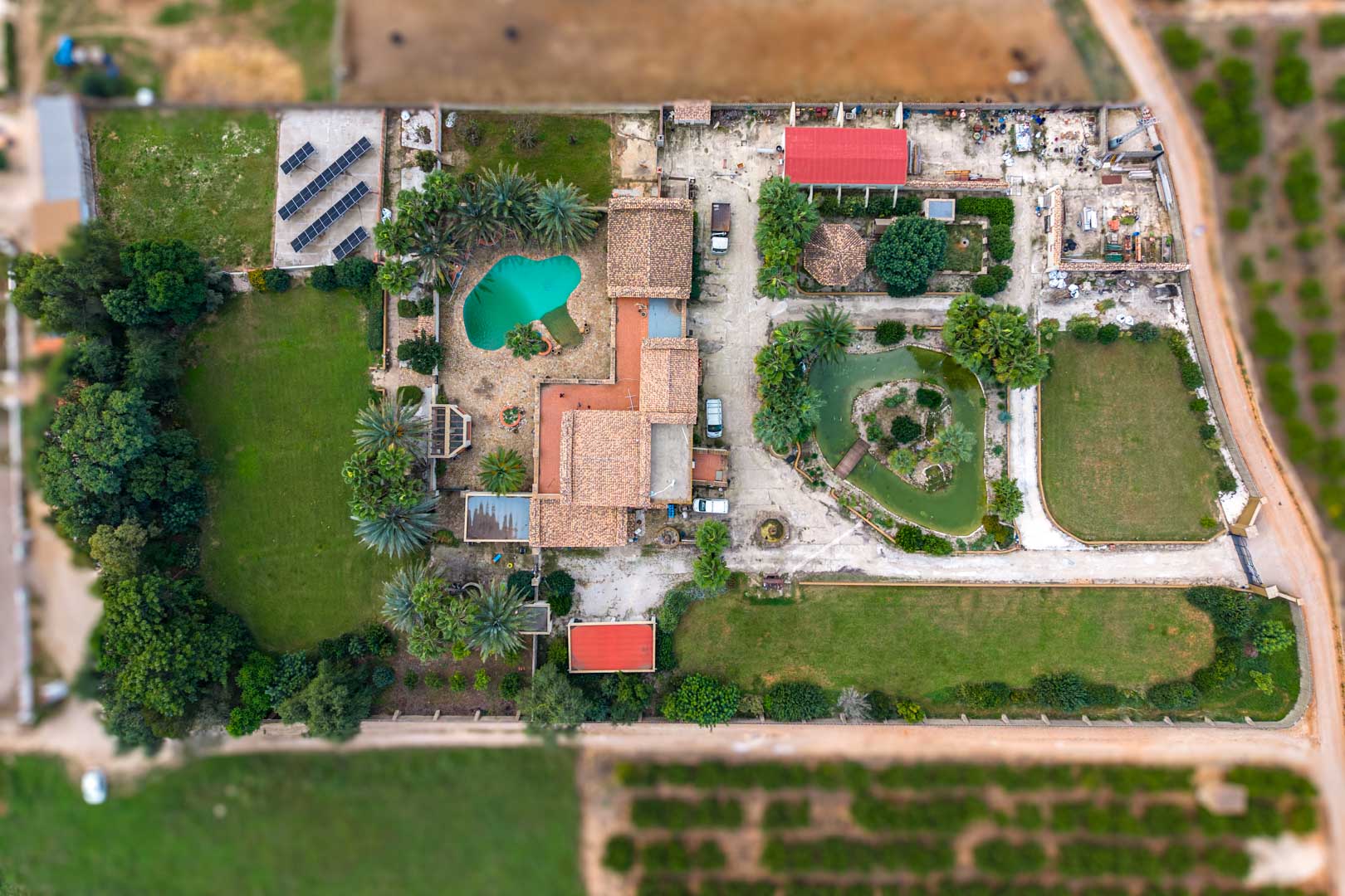Vista aérea cenital de la finca que muestra la casa principal, piscina, estanque japonés, amplios jardines y la instalación de placas solares en el terreno de 10.000 m2.