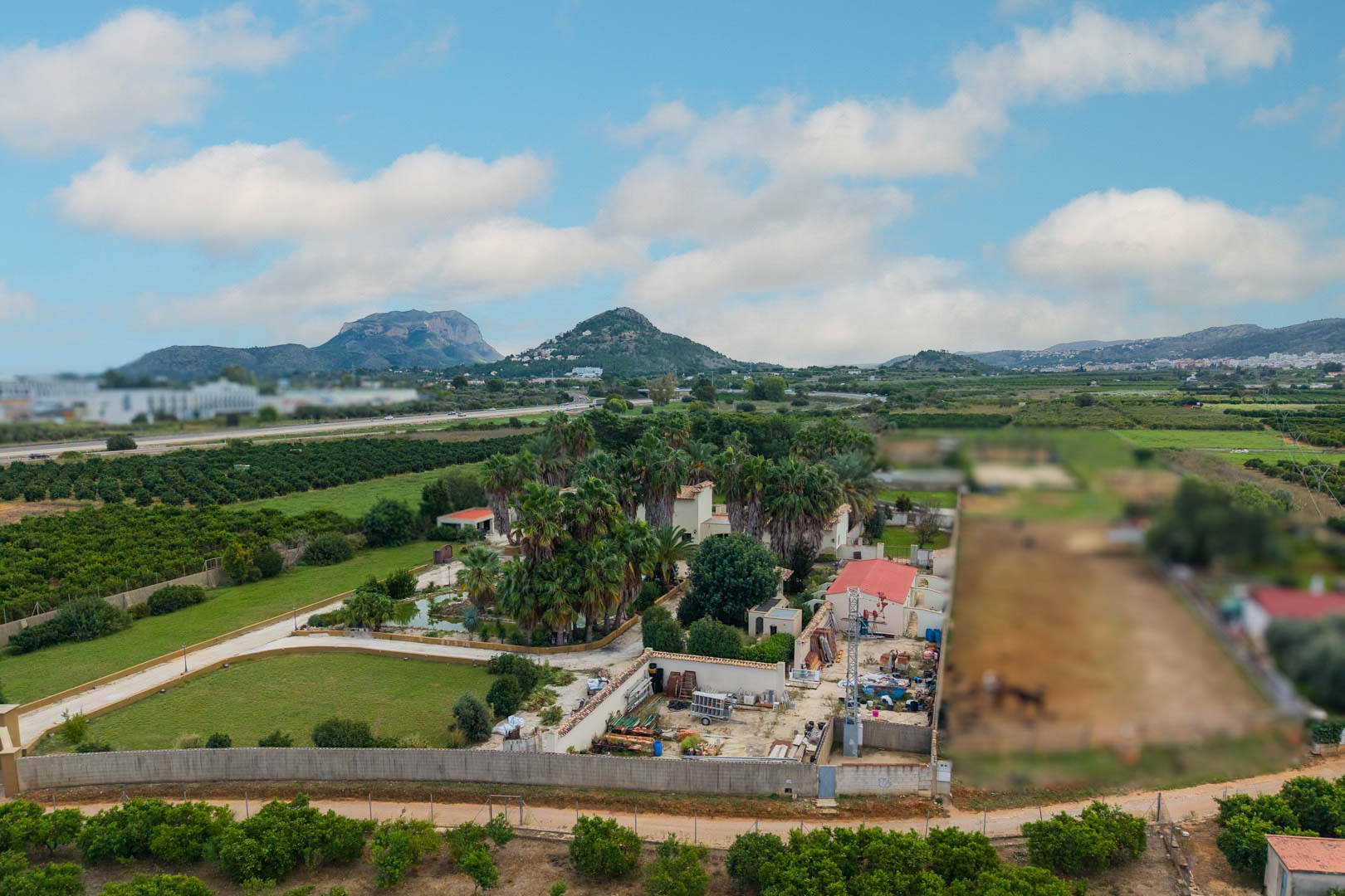 Vista aérea de la finca de 10.000 m2 en Ondara, destacando sus extensos jardines de palmeras, el estanque central y las vistas panorámicas hacia las montañas.