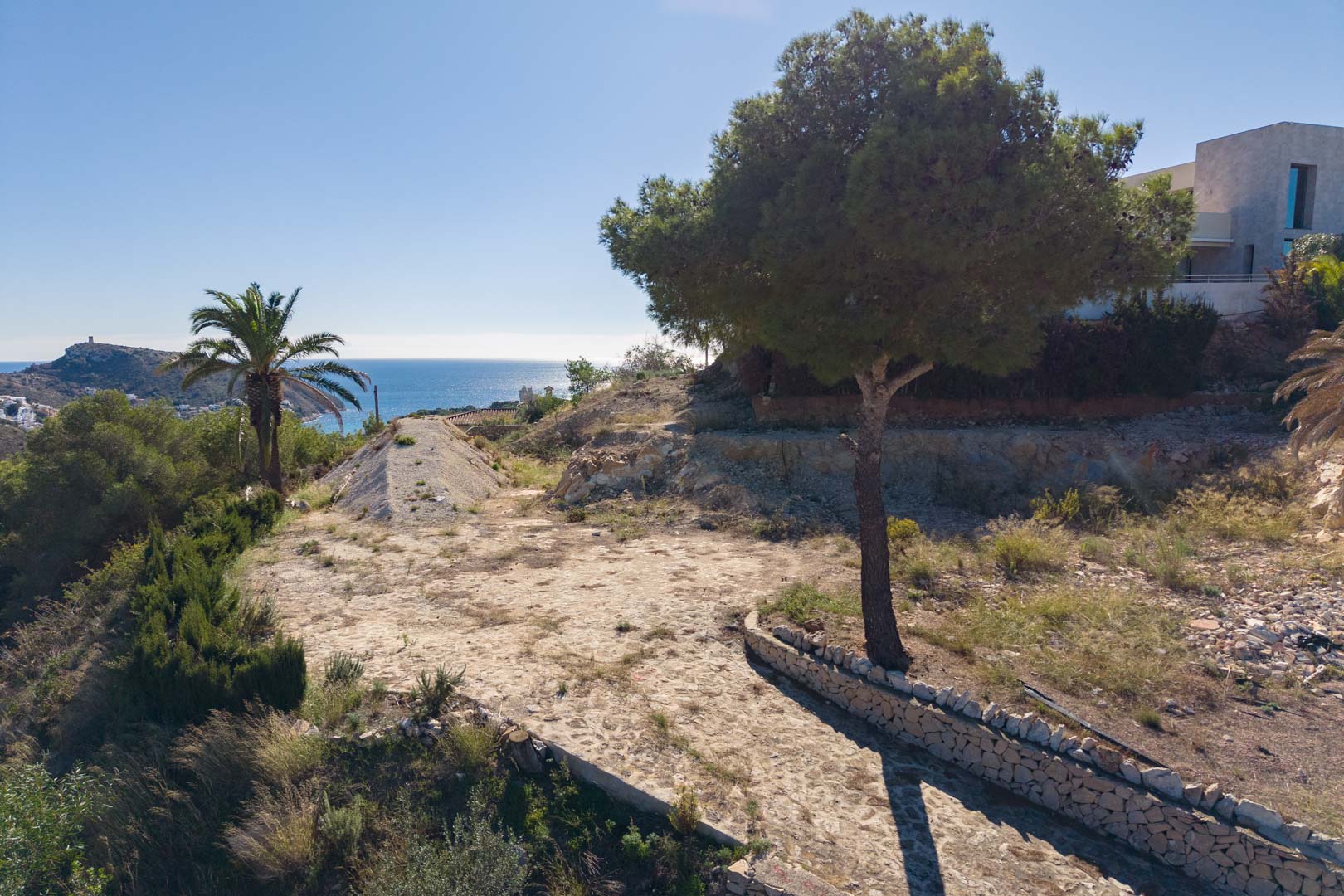 Vista exterior de la parcela con camino de piedra natural, vegetación mediterránea y vistas panorámicas al mar Mediterráneo en Moraira.