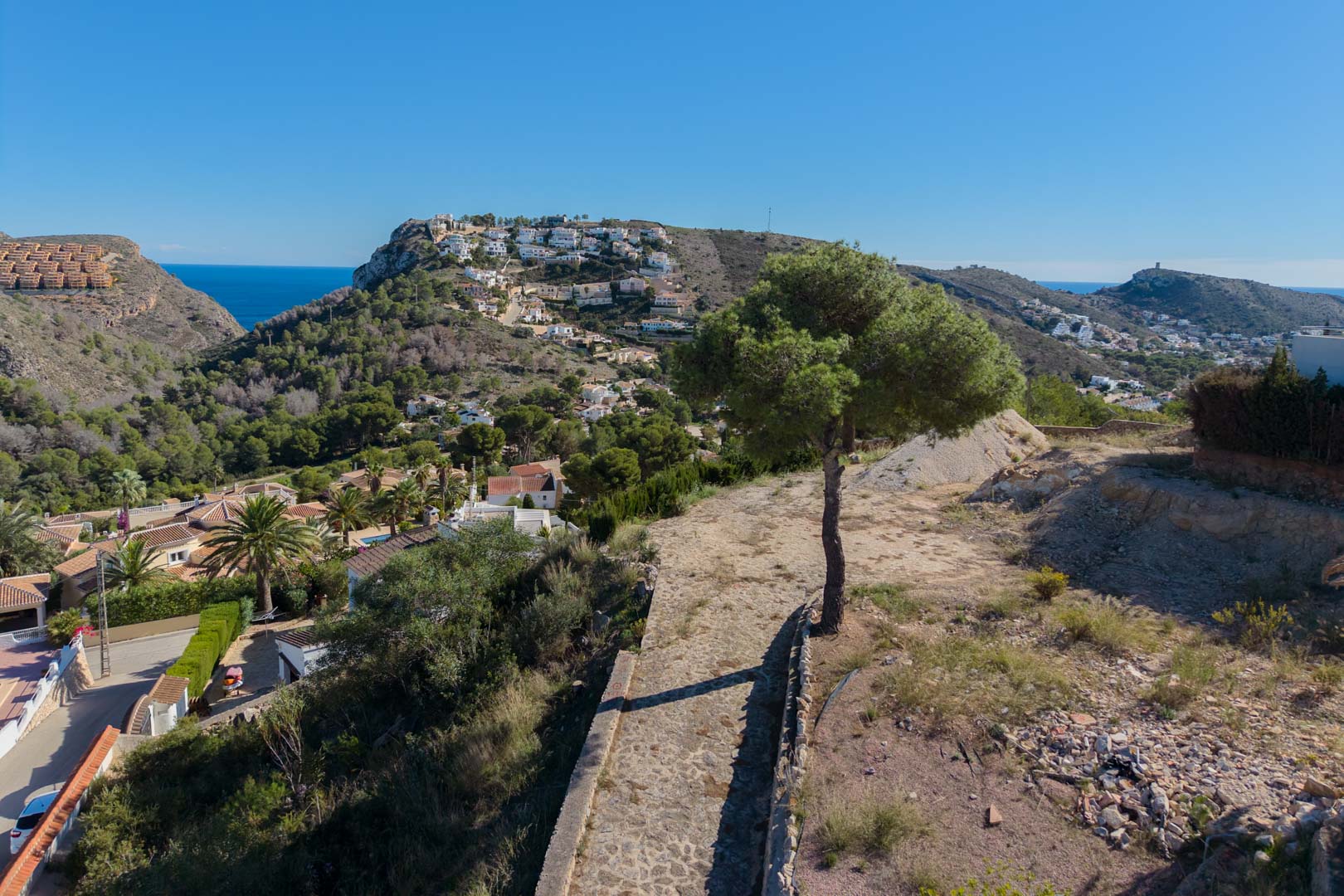 Vistas panorámicas desde la parcela elevada hacia el valle de Moraira y el mar Mediterráneo, rodeada de vegetación autóctona y pinos.