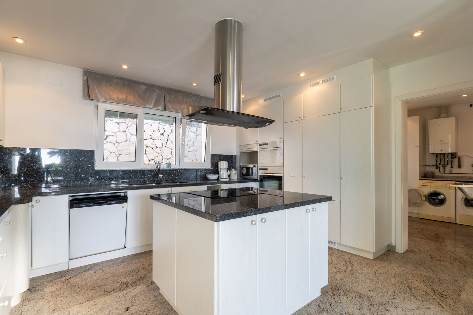 Cocina luminosa con isla central, encimera de granito azul y electrodomésticos modernos integrados.