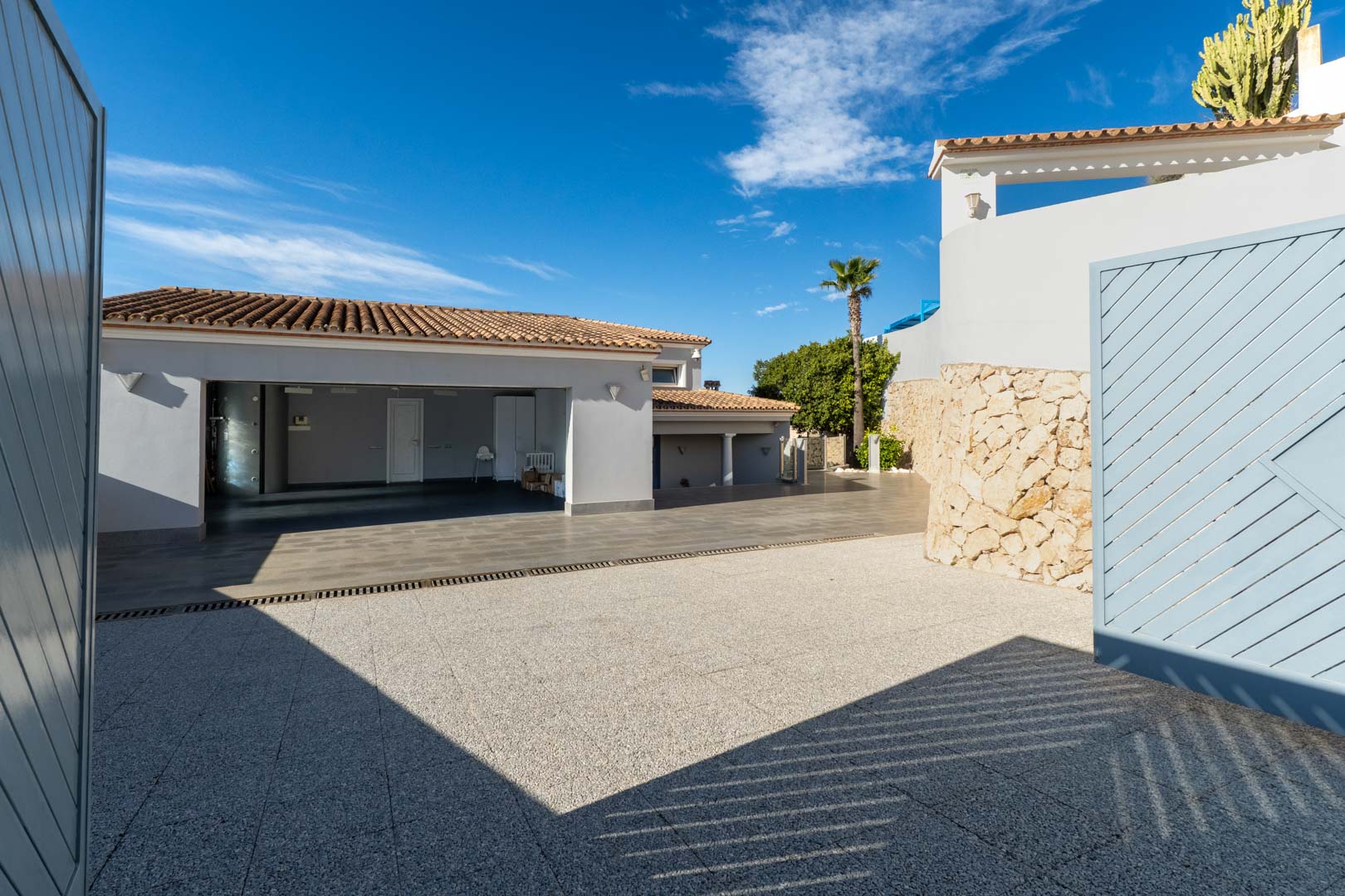 Entrada a la villa con garaje abierto y camino de grava bajo el cielo azul.