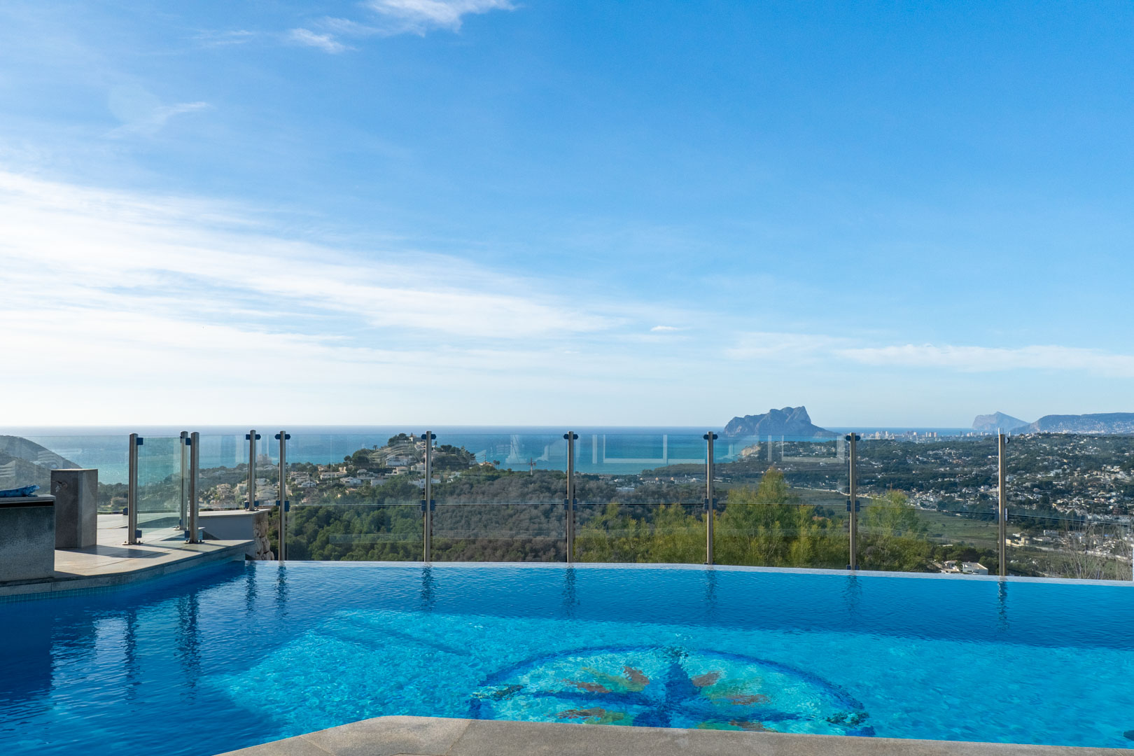 Piscina infinita con mosaico decorativo y vistas panorámicas al mar y la costa.