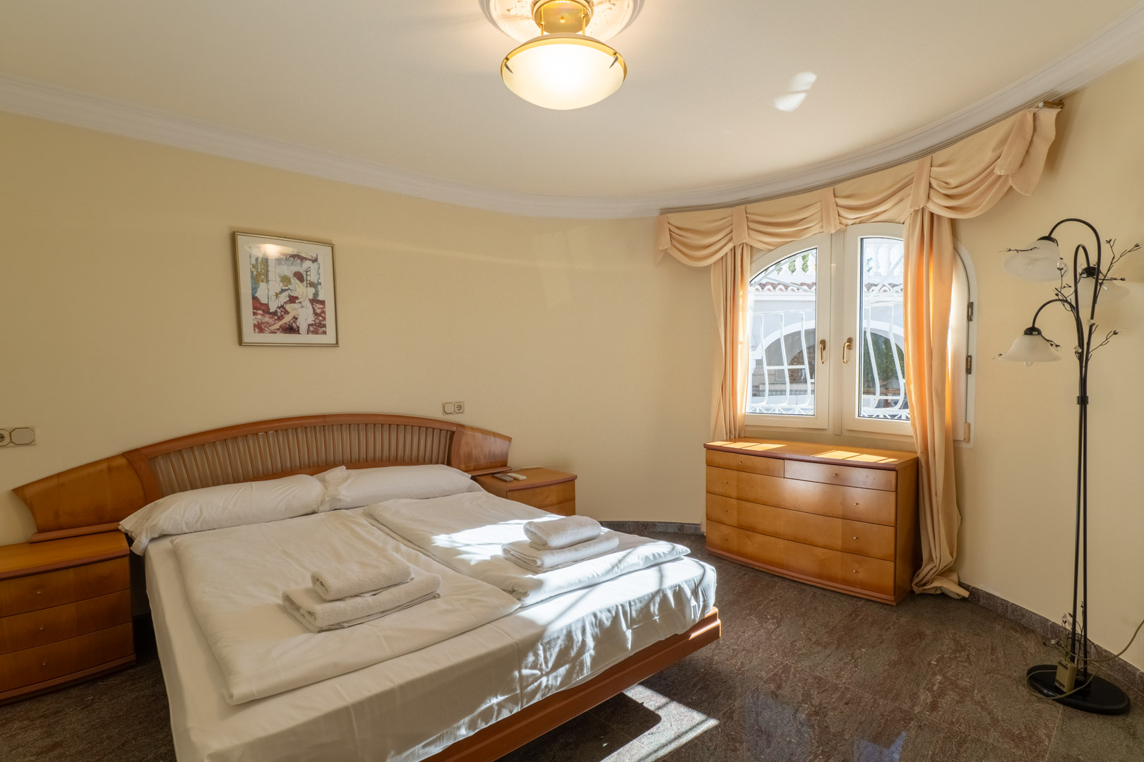 Dormitorio con mobiliario de madera integrada, suelos de granito y una ventana de arco que aporta luz natural a la estancia de paredes curvas.