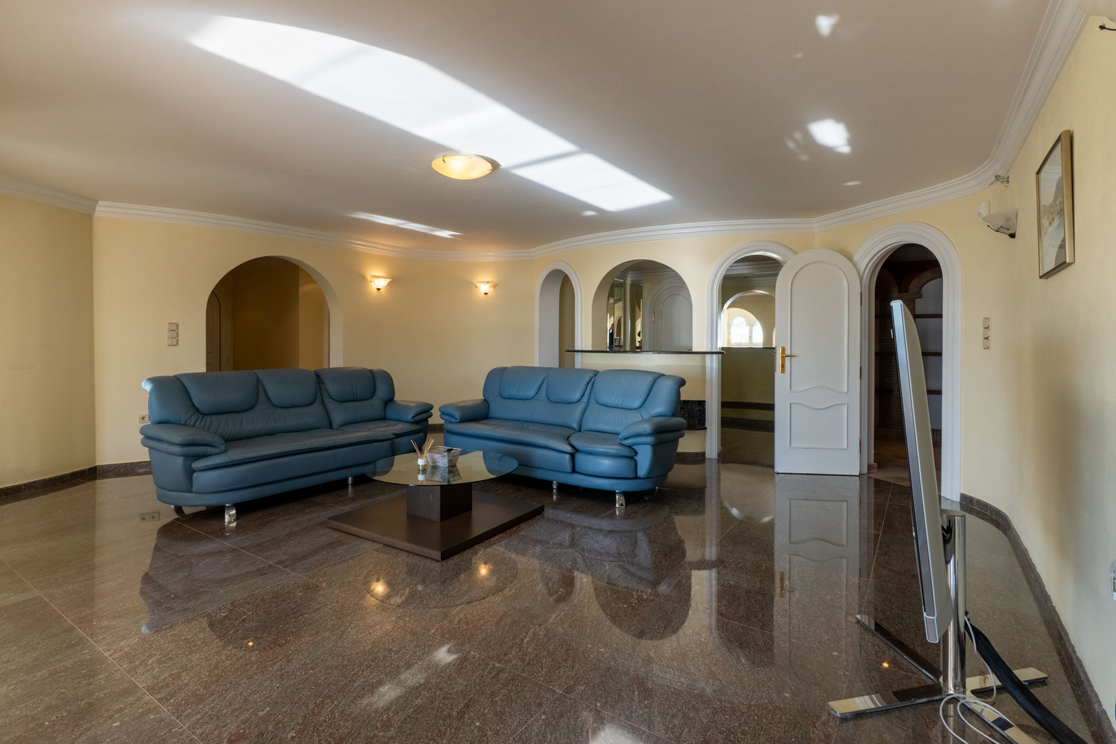 Salón con suelos de mármol brillante, sofás de piel azul y múltiples arcos decorativos que dan paso a una zona de bar y estancias contiguas.